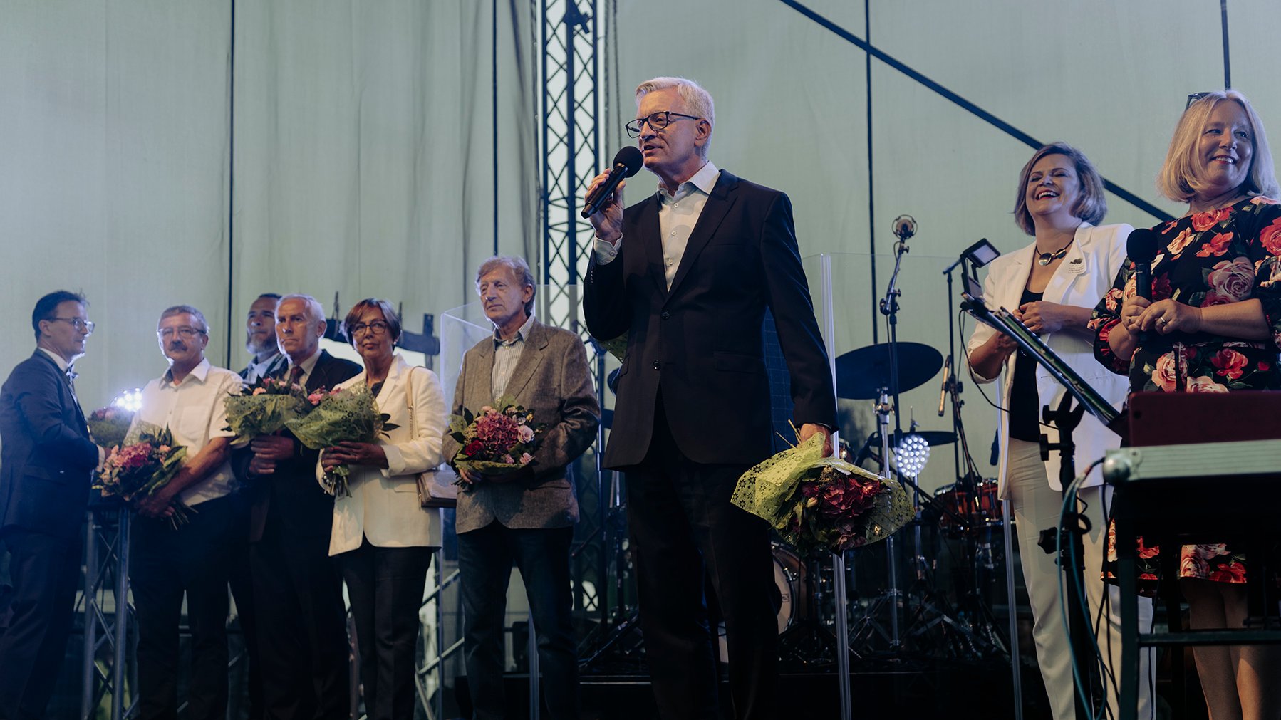 Scena, na niej osiedlowi radni i Jacek Jaśkowiak, prezydent Poznania, mówiący do mikrofonu