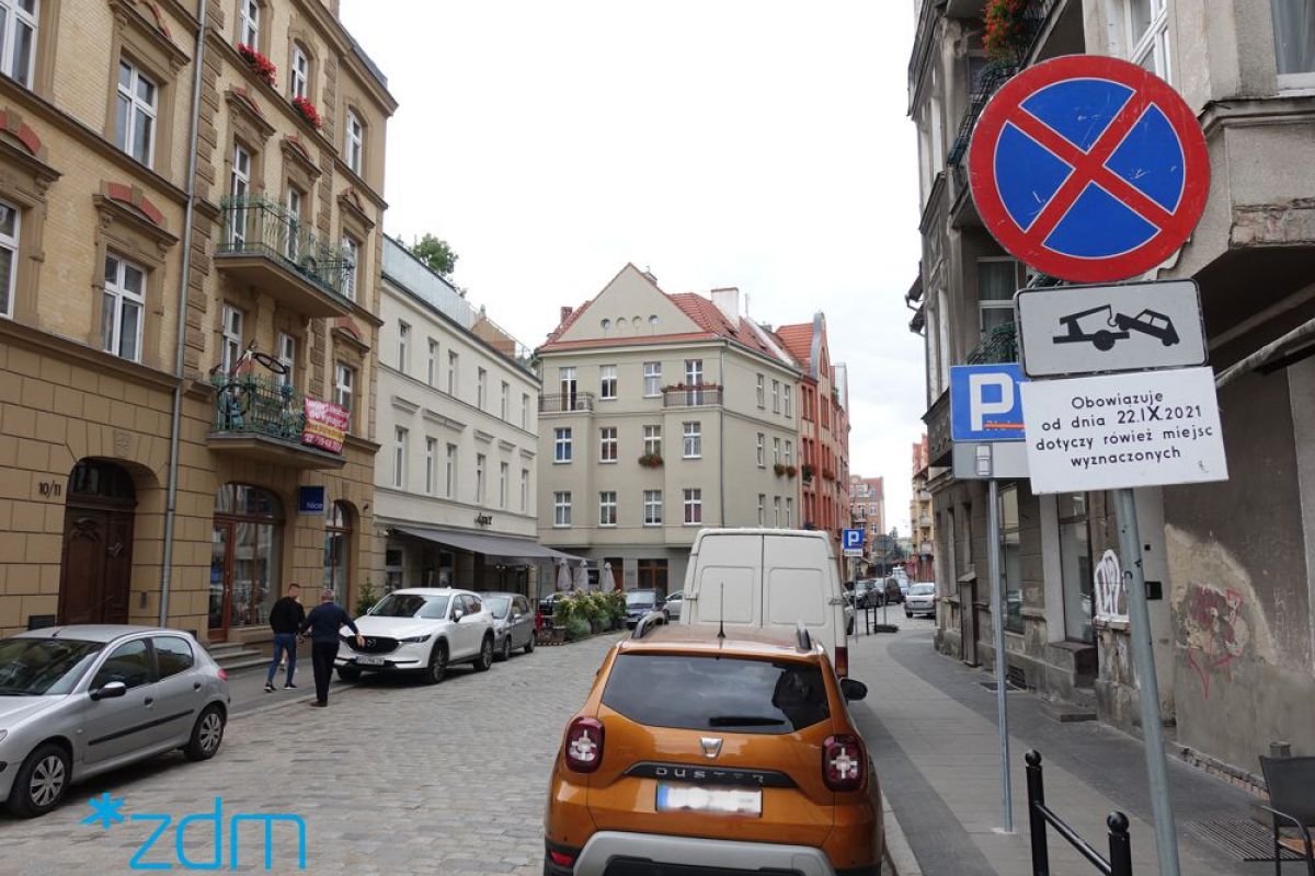 Zdjęcie pokazuje ulicę na Śródce, gdzie postawiono oznakowanie informujące o zmianie organizacji ruchu i konieczności przeparkowania aut na czas prac - grafika artykułu