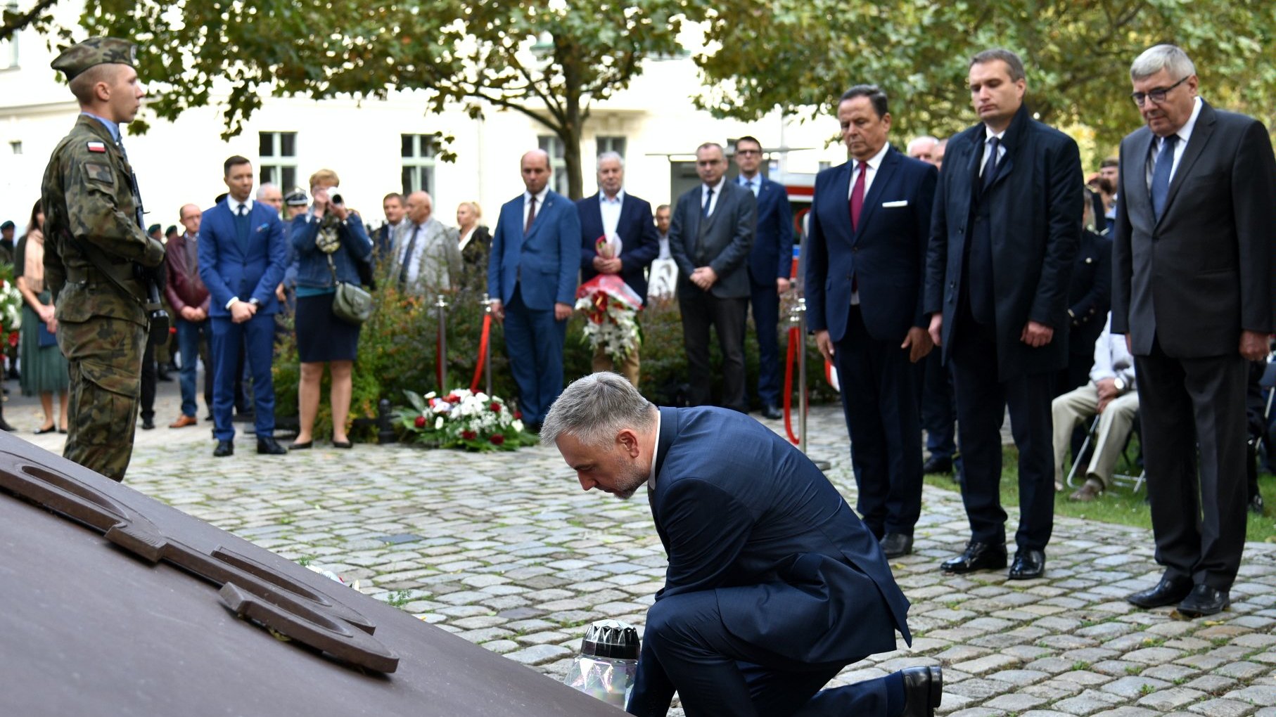 Zdjęcie przedstawia marszałka kładącego znicz pod pomnikiem, za nim stoją przedstawiciele władz samorządowych.