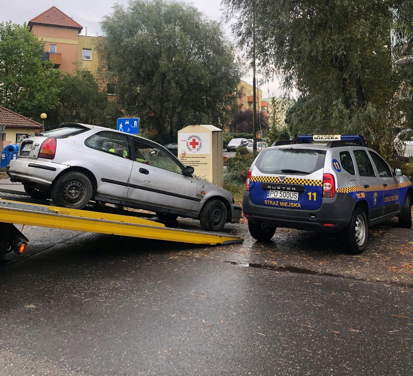 Zdjęcie przedstawia holowany samochód wciągany na lawetę. Obok znajduje się auto straży miejskiej. - grafika artykułu