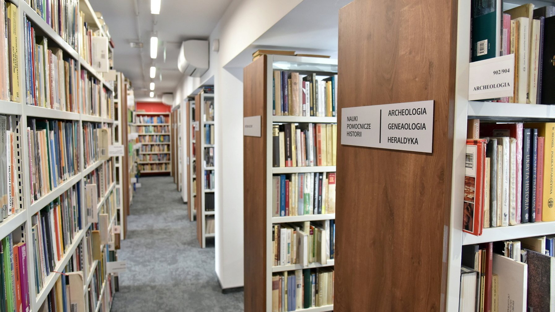 Zdjęcie przedstawia wnętrze biblioteki. Widać na nim półki z książkami.