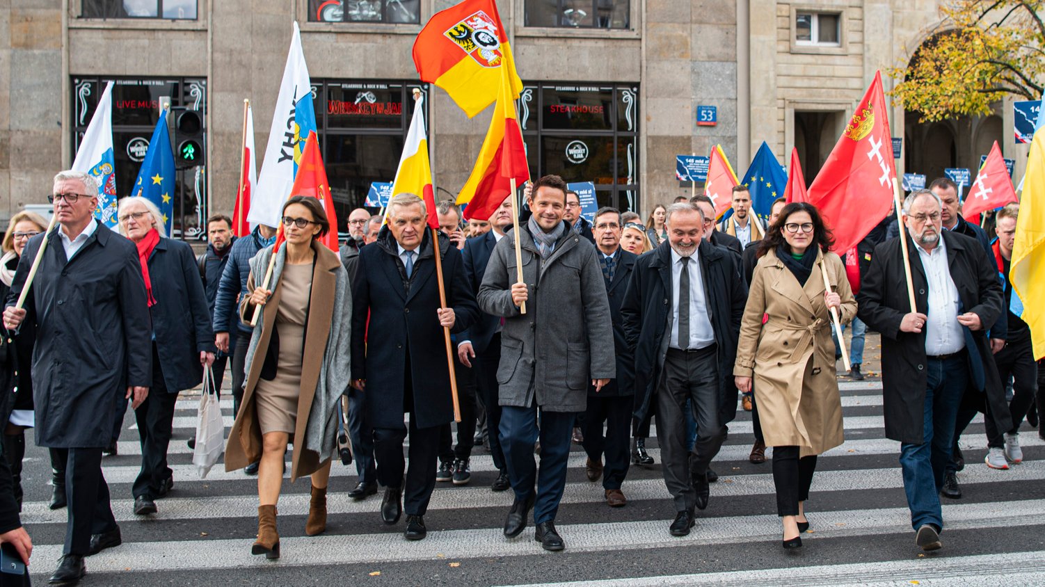 Na zdjęciu samorządowcy z flagami swoich miejscowości, idą ulicą