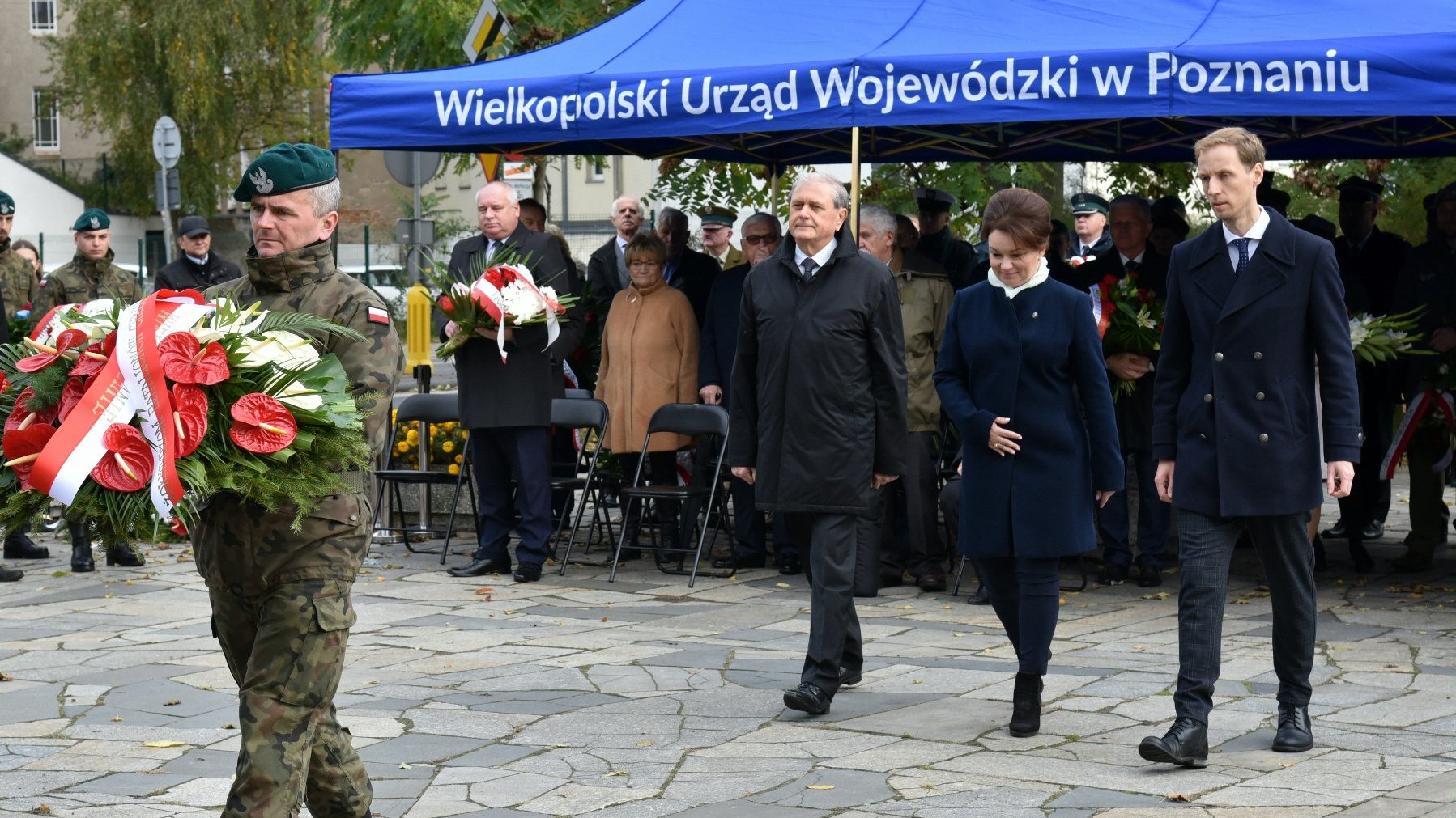 Na zdjęciu przedstawiciele władz miasta i województwa obok siebie, przed nimi żołnierz trzymający wiązankę kwiatów