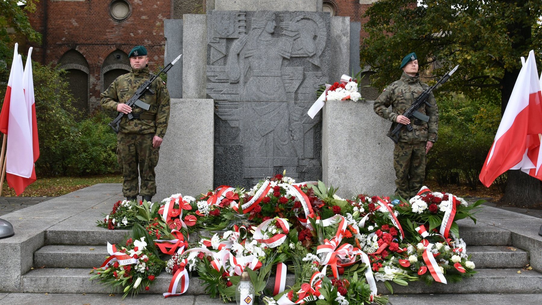 Na zdjęciu pomnik, obok niego żołnierze trzymający wartę honorową, pod pomnikiem złożone wiązanki