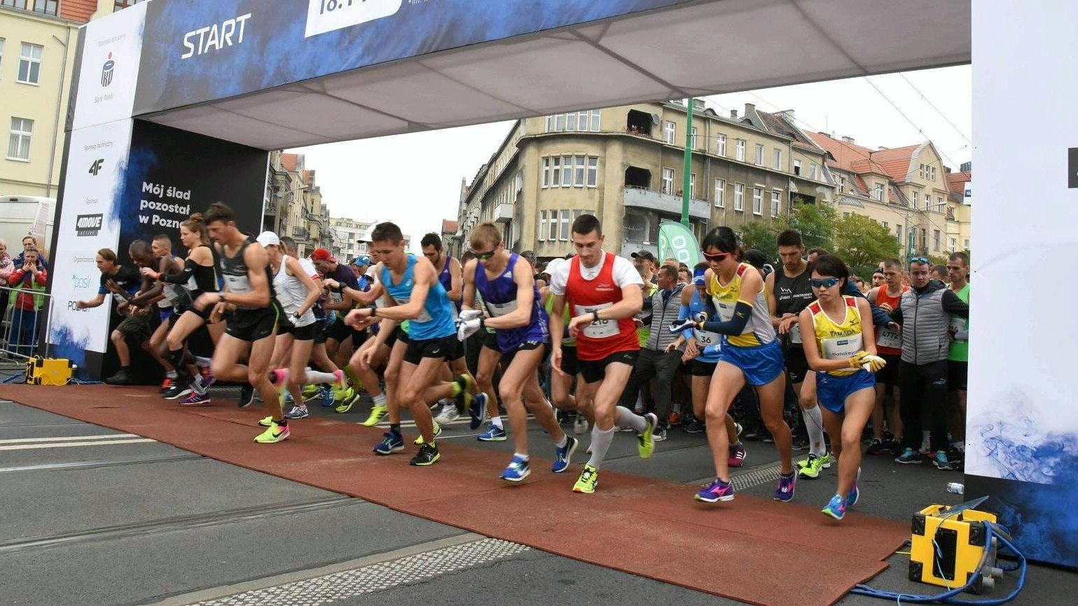 Na zdjęciu start poznańskiego biegu, na starcie dziesiątki biegaczy, którzy właśnie rozpoczynają bieg - grafika artykułu