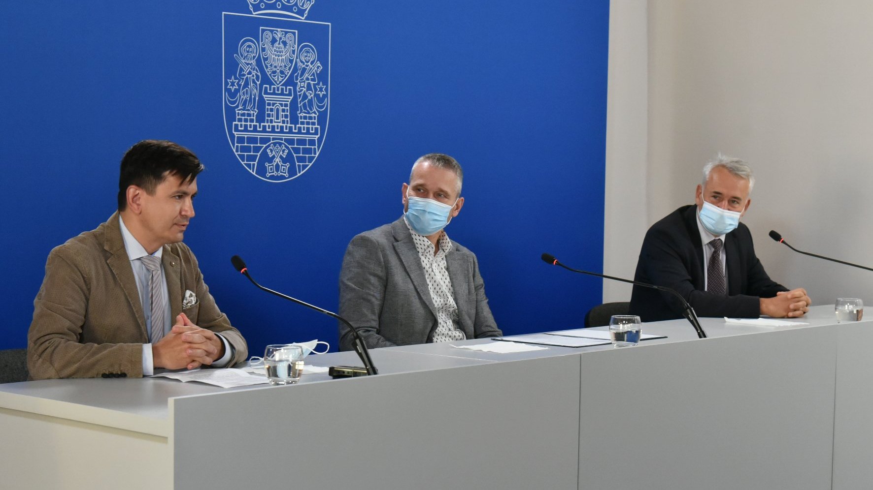 Na zdjęciu trzej mężczyźni za stołem konferencyjnym, w tle granatowa ścianka z herbem miasta, na pierwszym planie Przemysław Foligowski, dyrektor Wydziału Oświaty