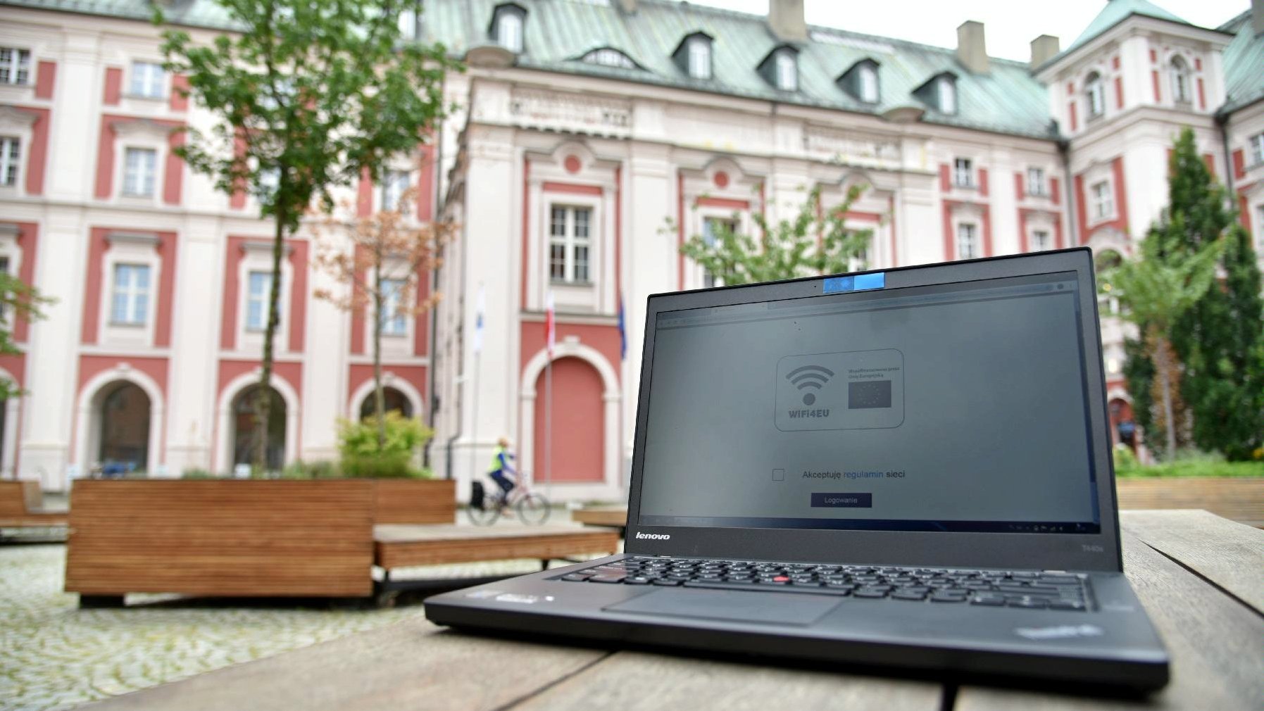 Na zdjęciu dziedziniec urzędu miasta, w tle budynek urzędu, na pierwszym planie otwarty laptop