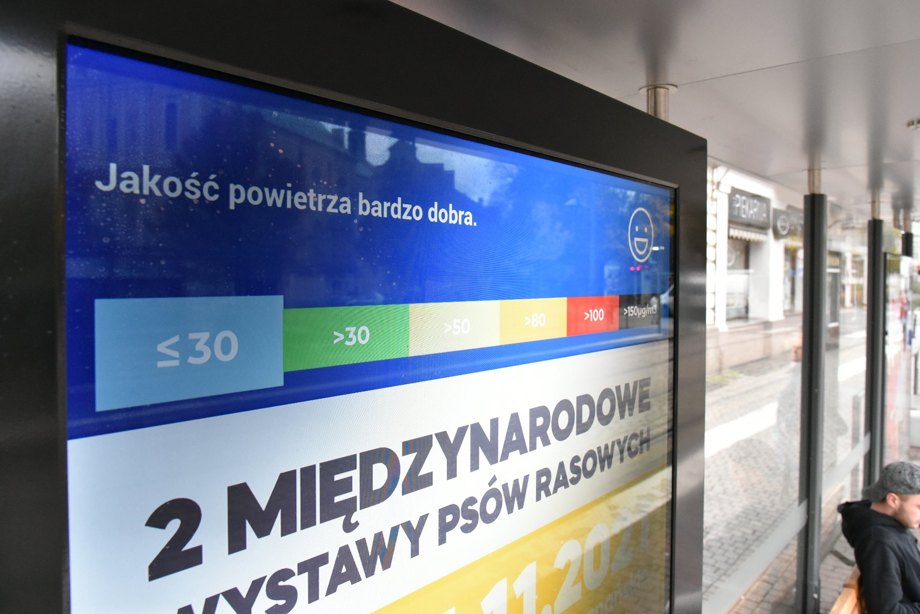 Galeria zdjęć przedstawia ekran z reklamą i informacją o jakości powietrza, znajdujący się na przystanku komunikacji miejskiej. - grafika artykułu