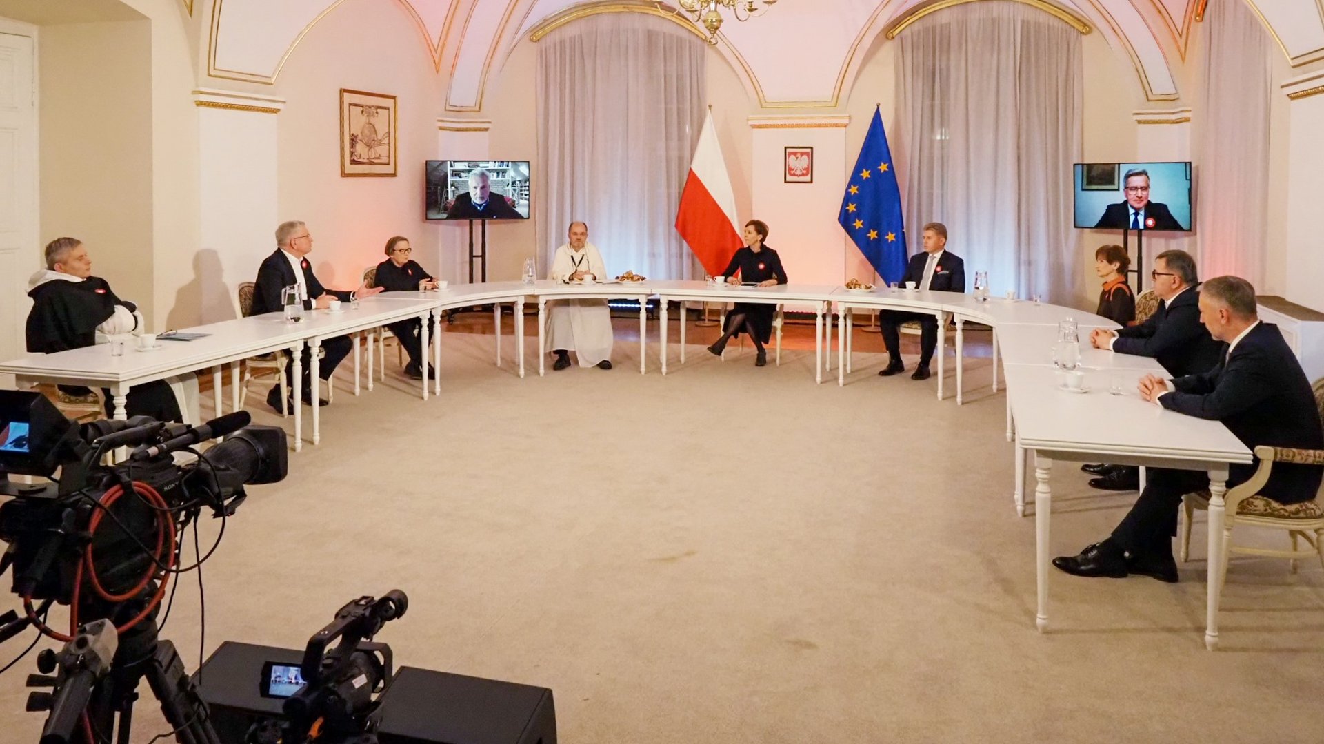 Sala Biała Urzędu Miasta, przy stole siedzą uczestnicy debaty, za nimi flagi Polski i UE - grafika artykułu