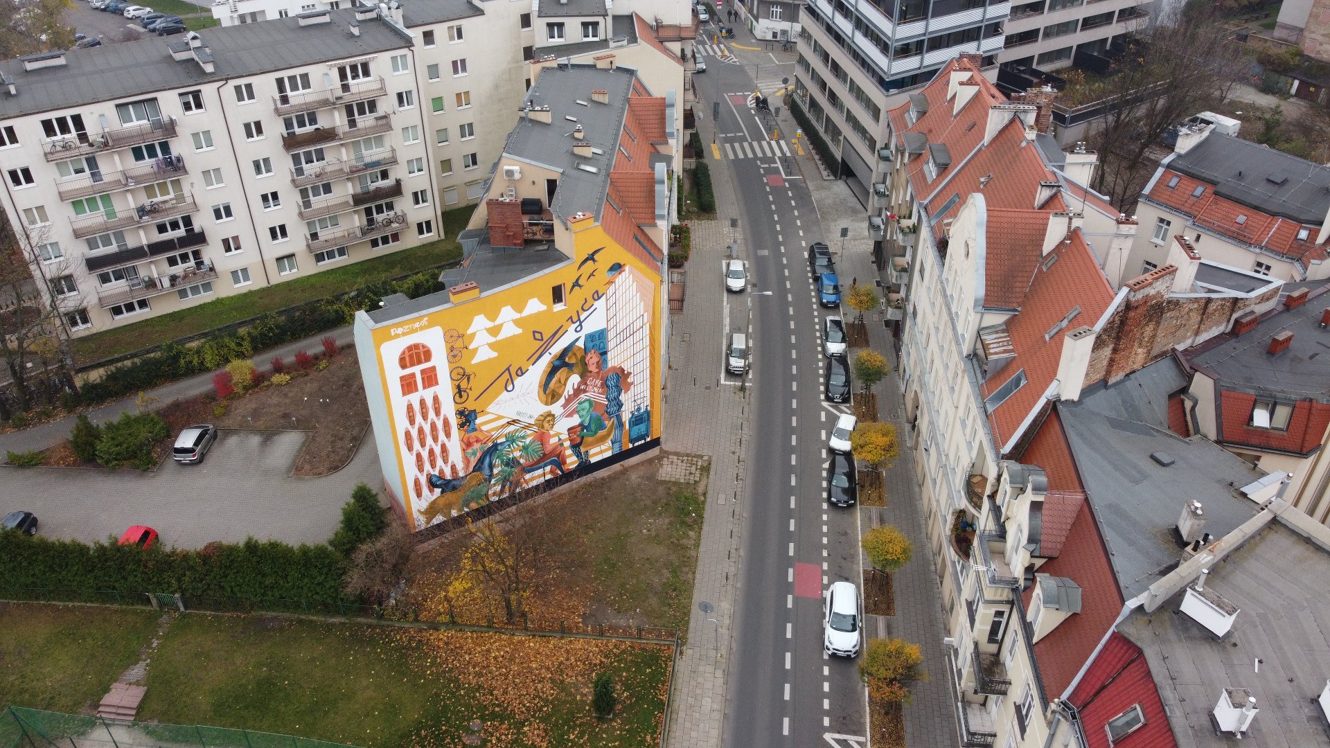 Galeria zdjęć przedstawia nowy mural na Jeżycach. Widać na nim m.in. dwóch poetów Słowackiego i Mickiewicza. Obok znajduje się ulica z samochodami.