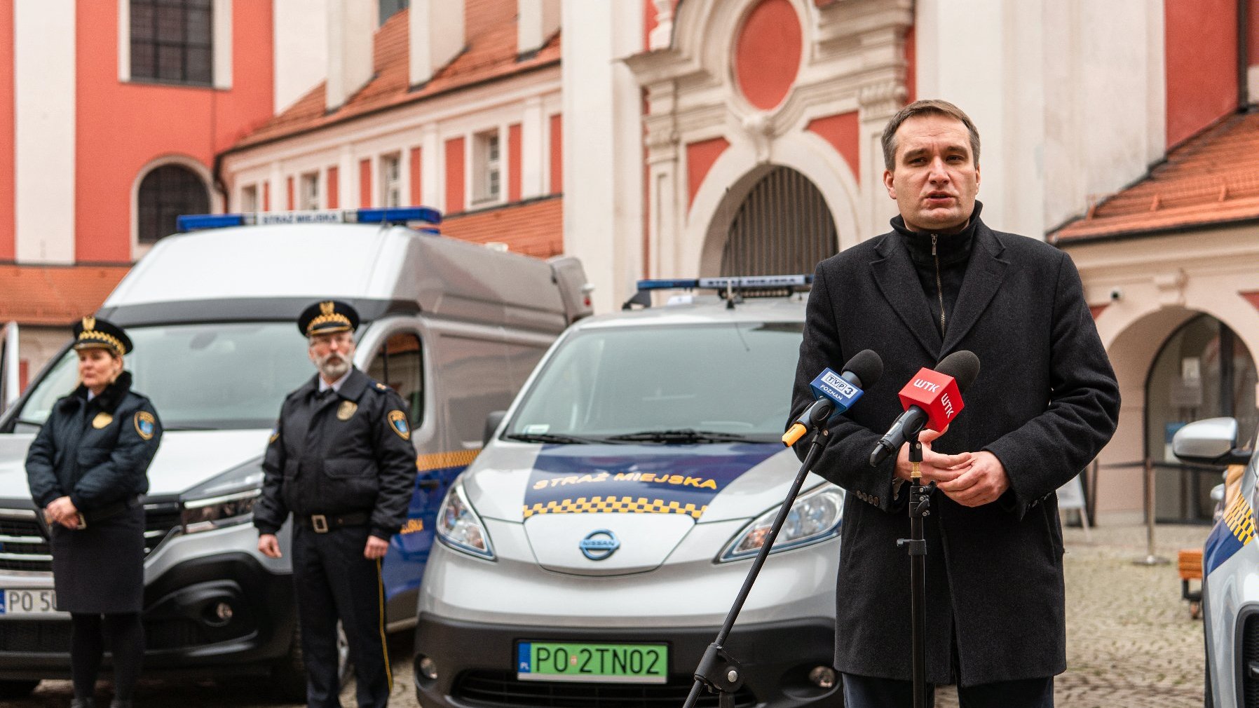 Galeria zdjęć przedstawia uczestników konferencji prasowej na dziedzińcu urzędu miasta. W tle widać nowe samochody.