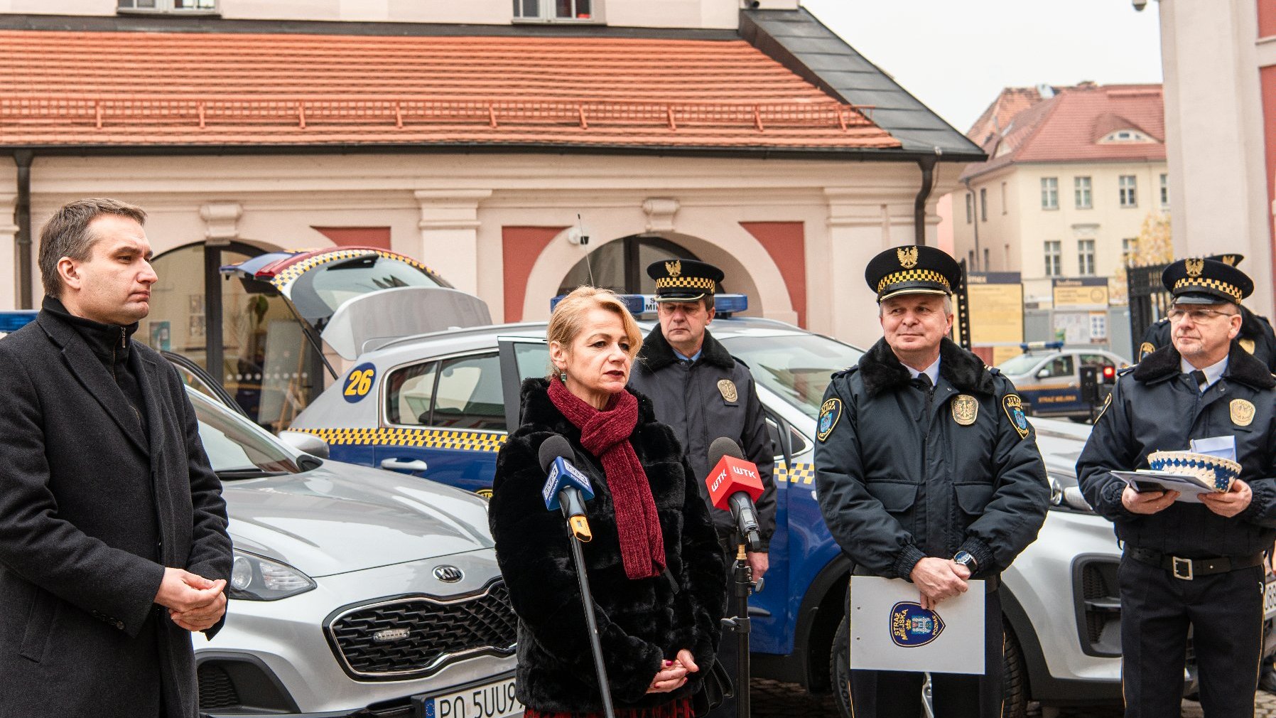 Galeria zdjęć przedstawia uczestników konferencji prasowej na dziedzińcu urzędu miasta. W tle widać nowe samochody.