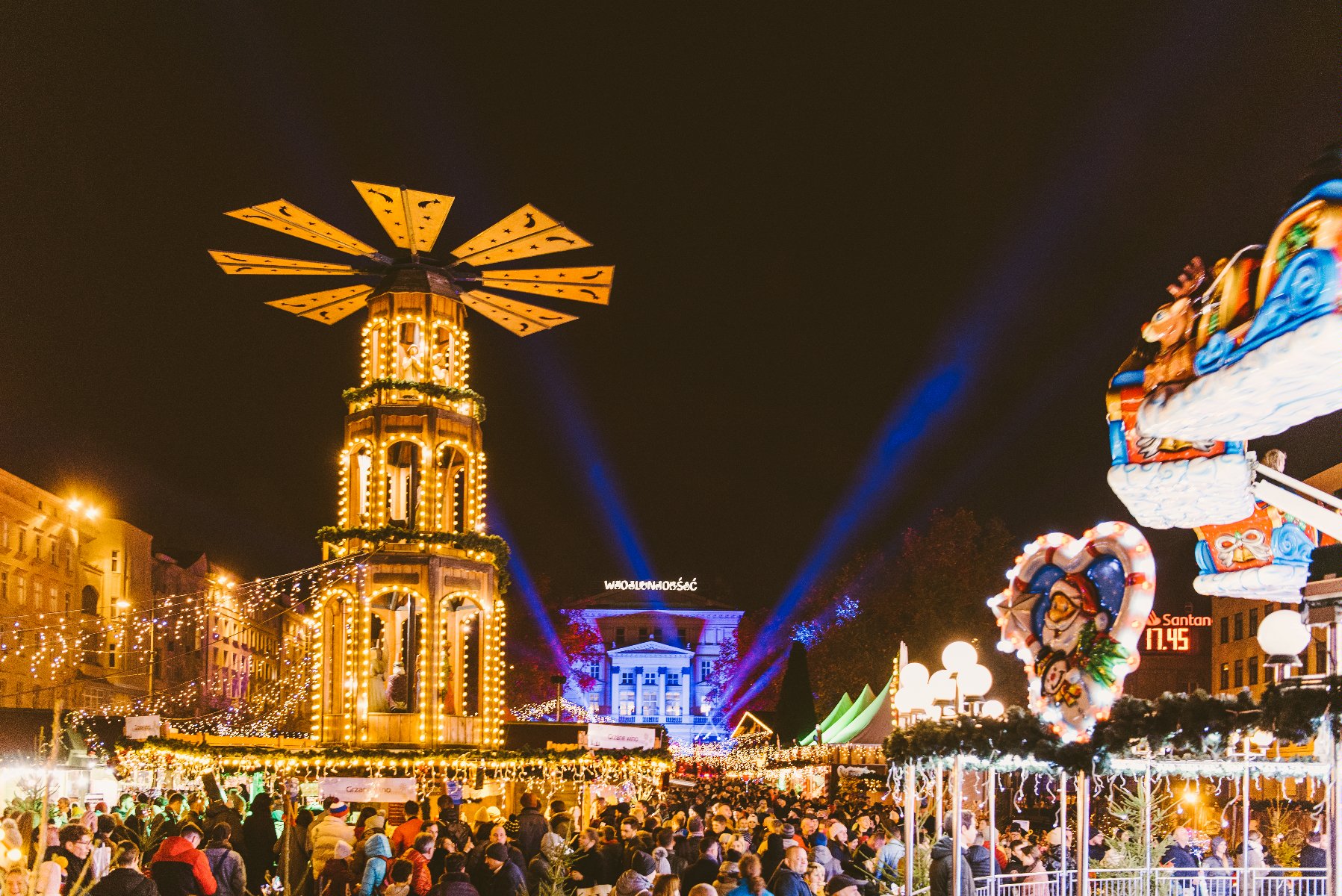 Zdjęcie przedstawia plac Wolności, na którym trwa Betlejem Poznańskie. Widać na nim m.in. karuzelę, podświetlony budynek Arkadii, nad którym wisi neon z napisem "Wolność" oraz tłum ludzi. - grafika artykułu