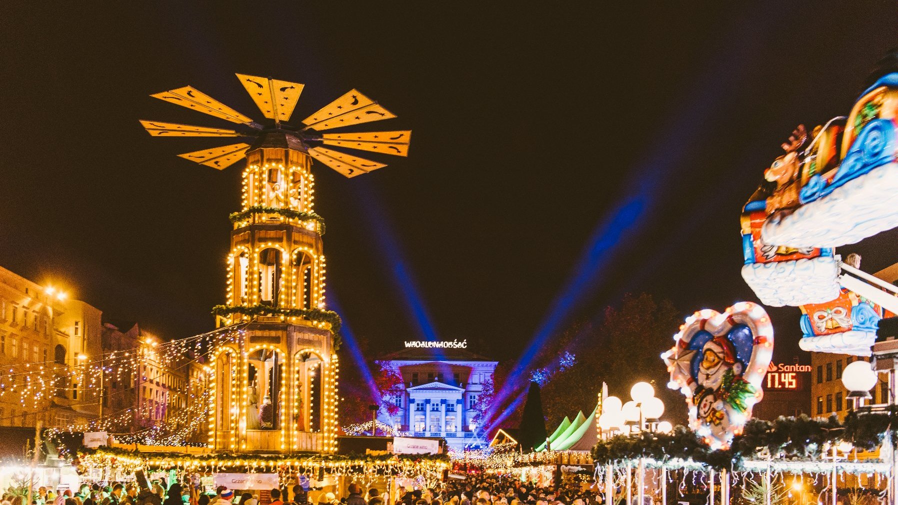 Zdjęcie przedstawia plac Wolności, na którym trwa Betlejem Poznańskie. Widać na nim m.in. karuzelę, podświetlony budynek Arkadii, nad którym wisi neon z napisem "Wolność" oraz tłum ludzi.