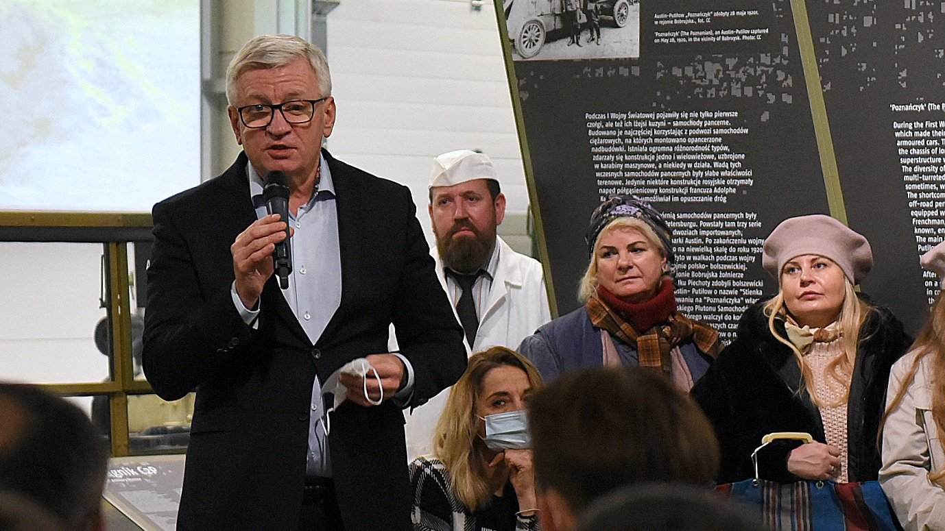 Na zdjęciu Jacek Jaśkowiak, prezydent Poznania, z mikrofonem w ręku, patrzy w obiektyw. Za nim grupa rekonstrukcyjna