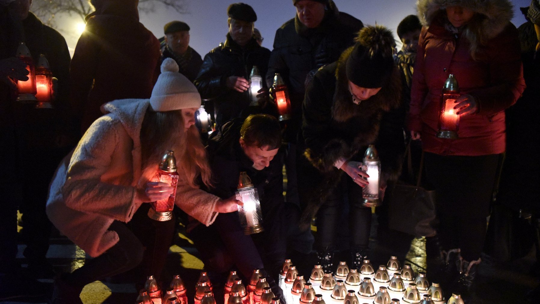 Grupa osób układa we flagę Polski białe i czerwone znicze.