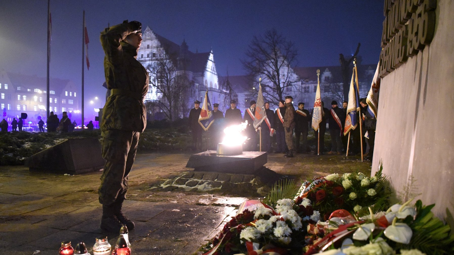 Salutujący żołnierz. W tle płonie znicz.