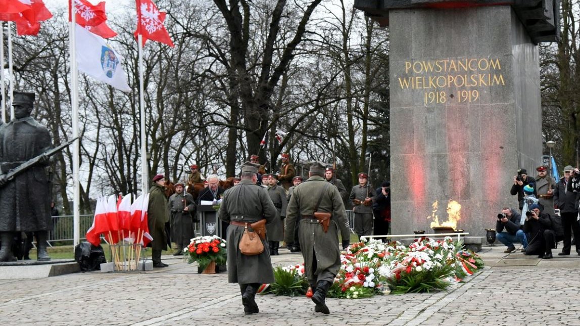 Zdjęcie przedstawia osoby składające kwiaty pod pomnikiem Powstańców Wielkopolskich. - grafika artykułu