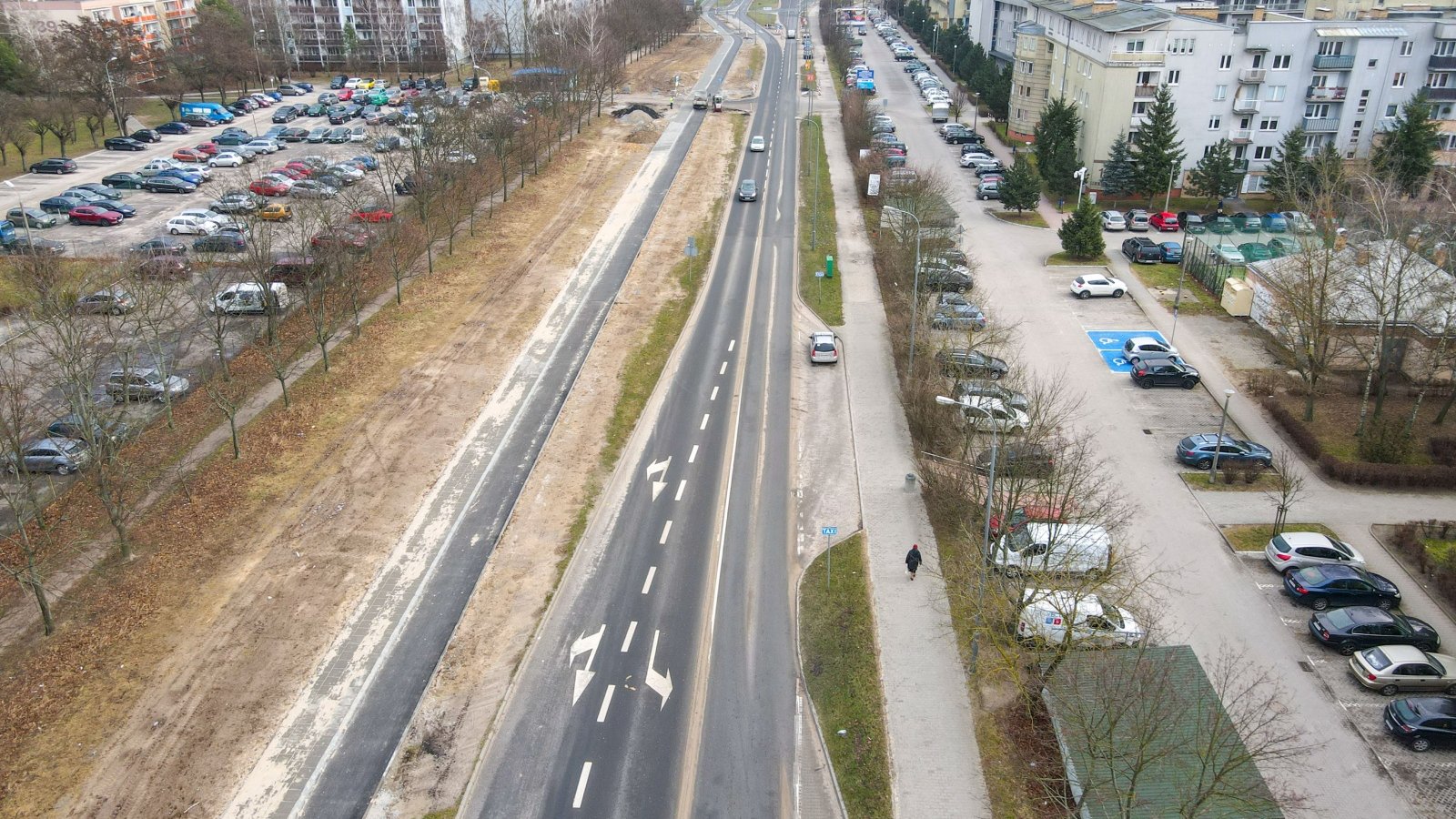 Na zdjęciu droga rowerowa widziana z lotu ptaka, po prawej bloki, po lewej parking