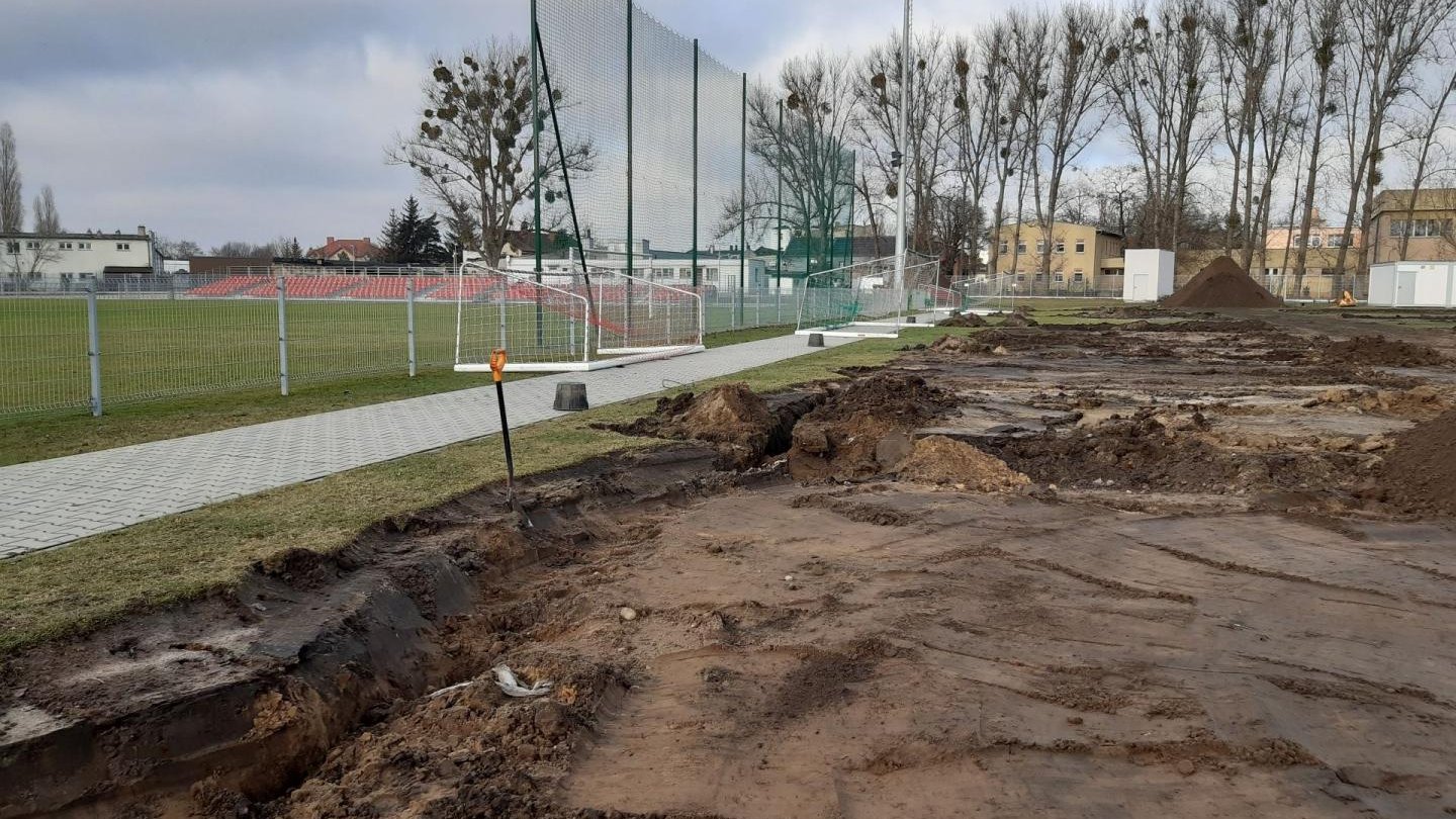 Galeria zdjęć przedstawia prace budowlane nad nowym boiskiem. Widać na nich hałdy ziemi, maszyny budowlane i pracowników.