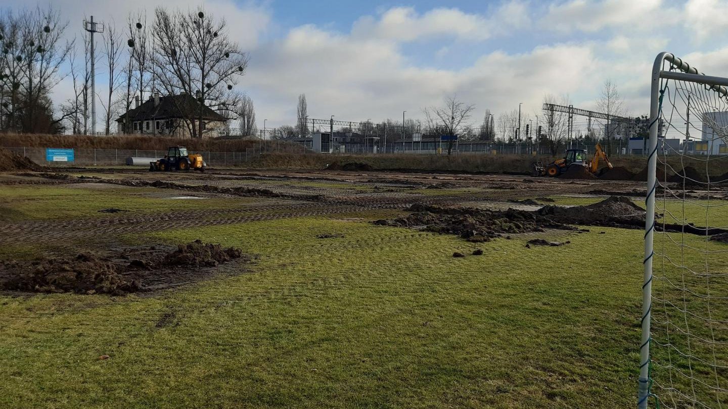 Galeria zdjęć przedstawia prace budowlane nad nowym boiskiem. Widać na nich hałdy ziemi, maszyny budowlane i pracowników.