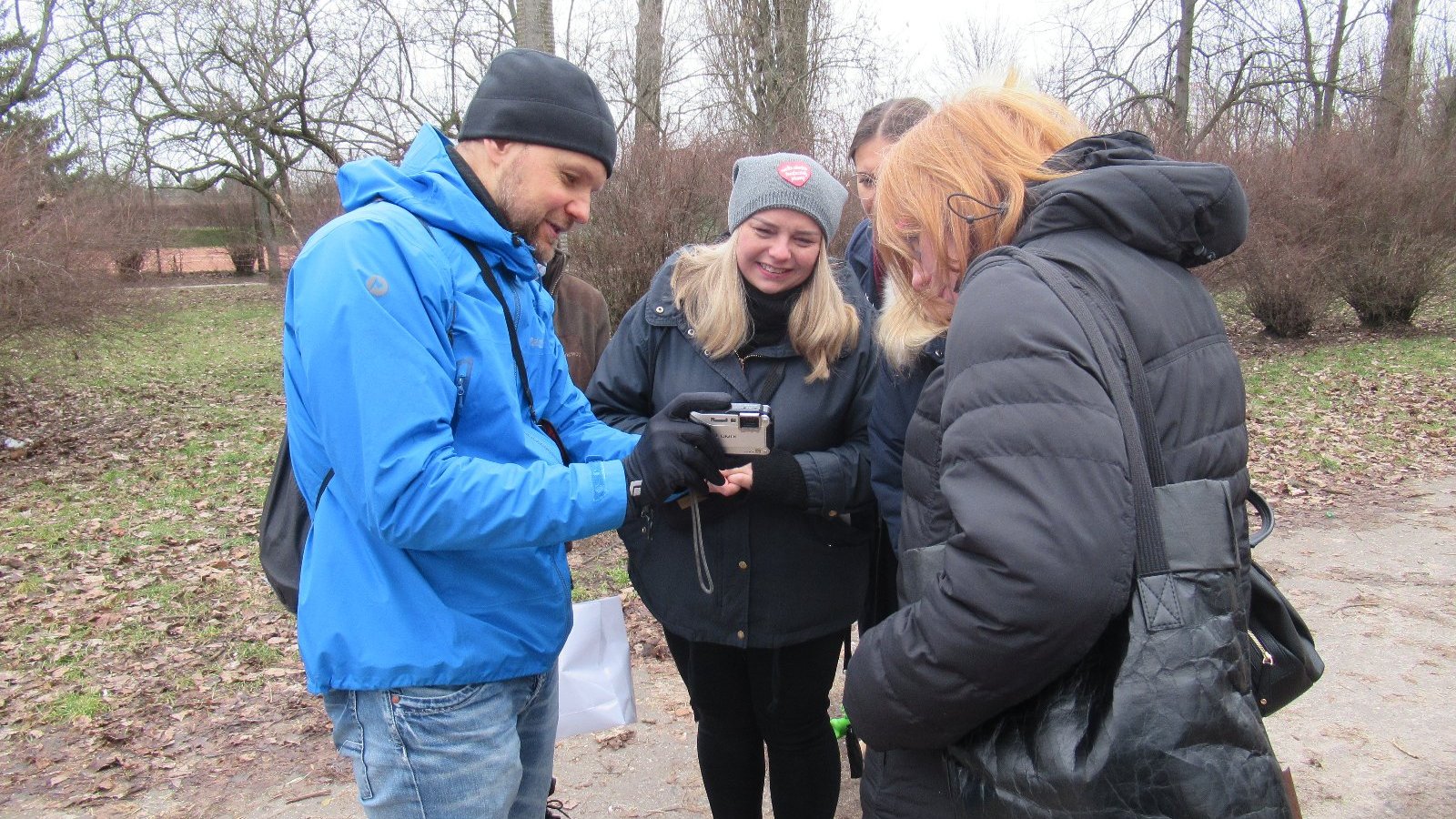 Zdjęcie przedstawia mężczyznę pokazującego coś kilku kobietą na ekranie aparatu fotograficznego.