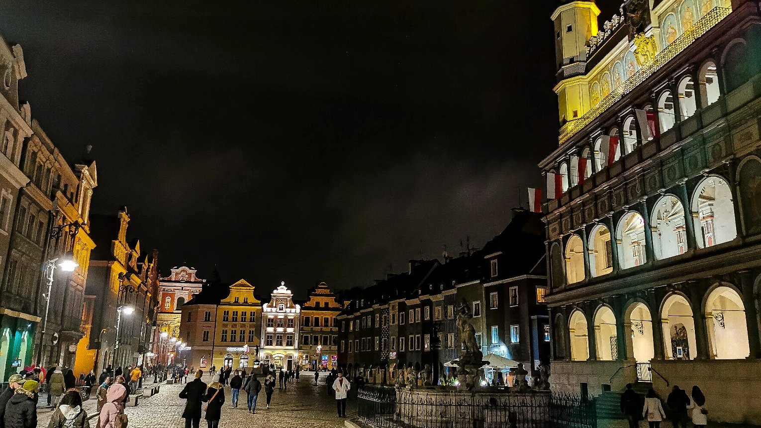 Zdjęcie przedstawia Stary Rynek po zmroku. Widać na nim budynki i spacerujących ludzi. - grafika artykułu