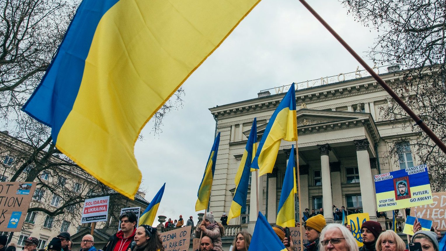 Na pierwszym planie grupa ludzi, flagi Ukrainy. W tle budynek Arkadii.