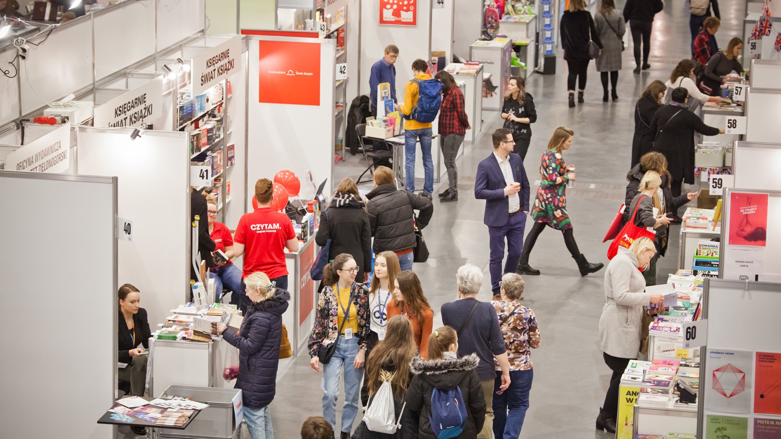 Galeria zdjęć przedstawia stoiska z książkami we wnętrzu hali targowej oraz oglądających je ludzi.