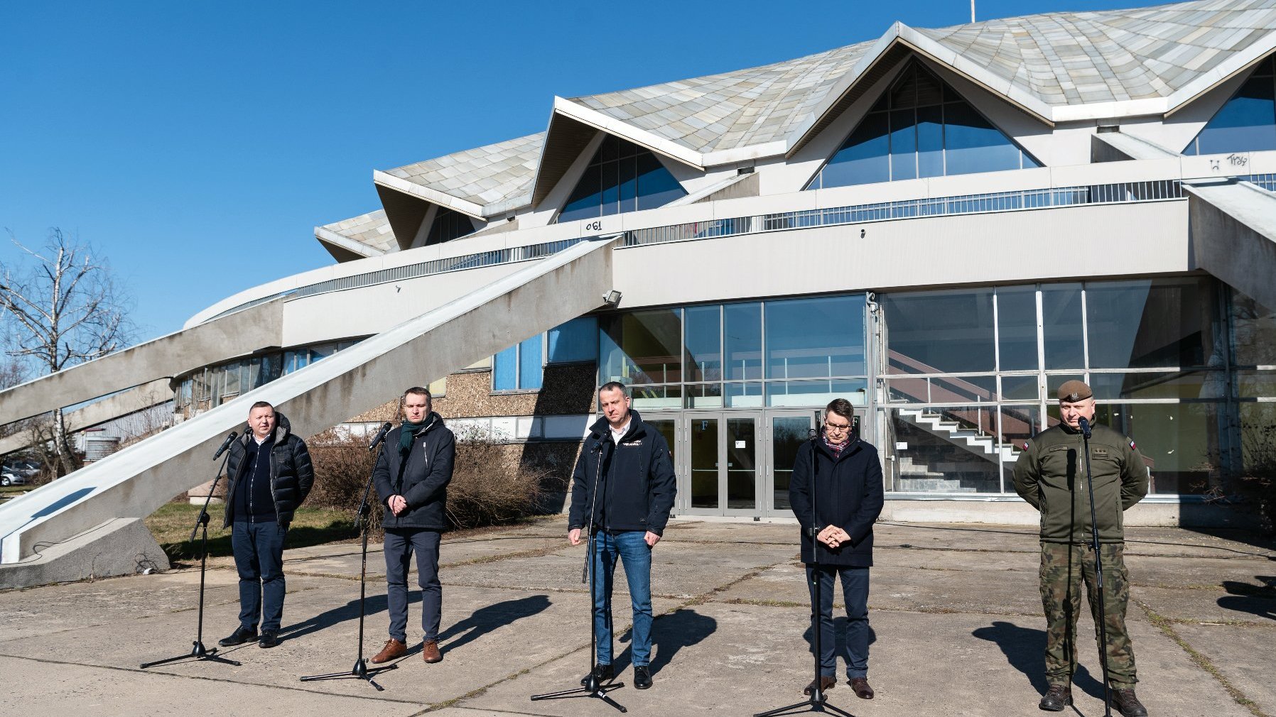 Grupa osób stoi przed halą Arena.