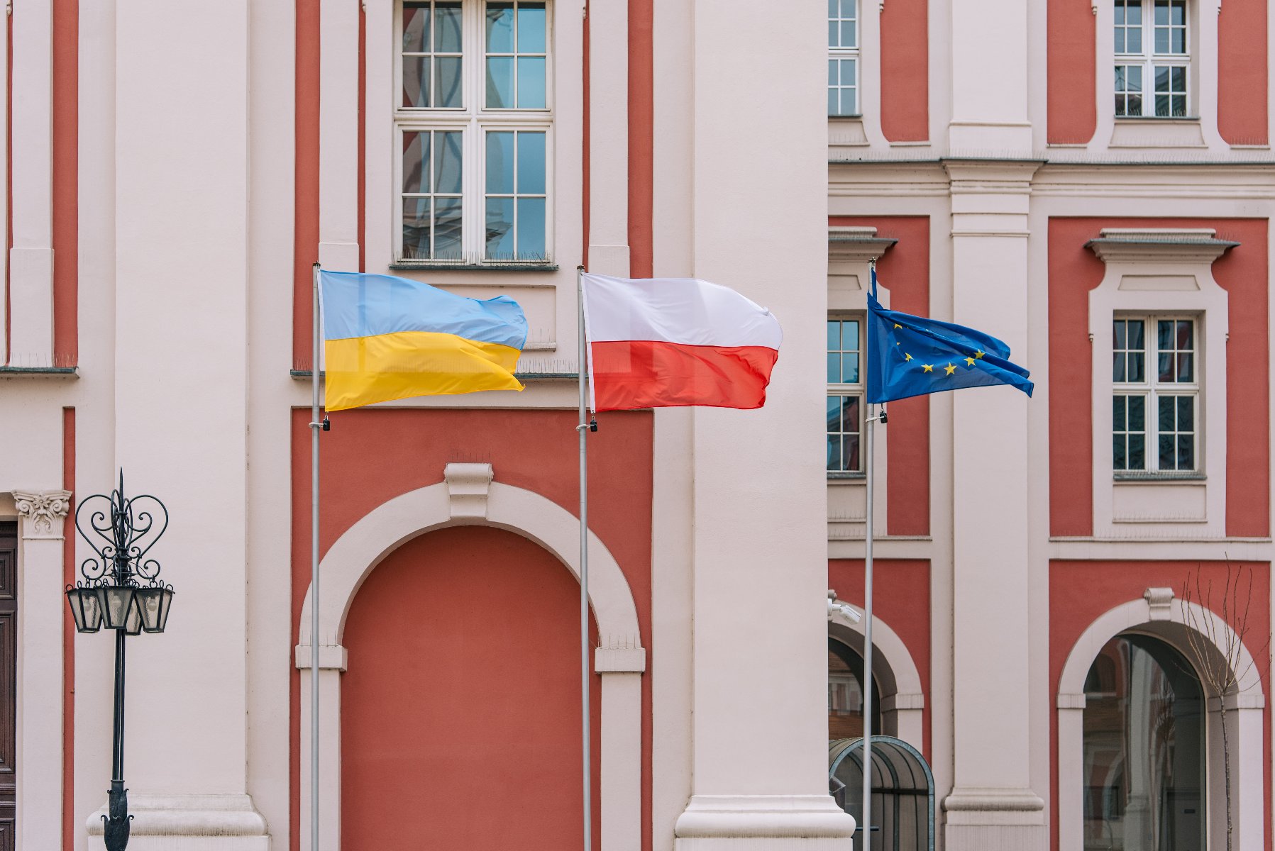 Na zdjęciu widać trzy flagi na tle budynku urzędu miasta. Od lewej: flaga Ukrainy, Polski i Unii Europejskiej. - grafika artykułu