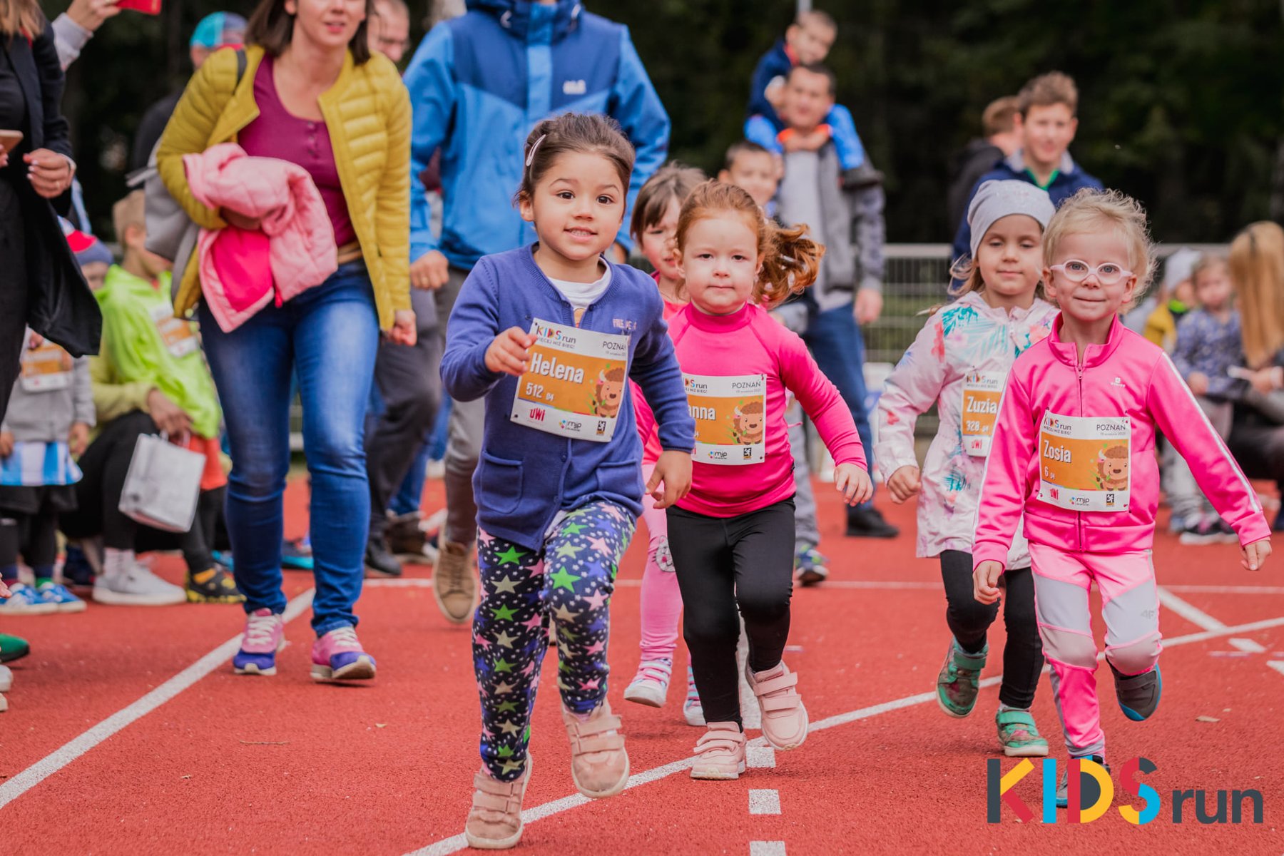 Galeria zdjęć przedstawia grupe dziecie biegnącą po bieżni podczas imprezy Kids Run. - grafika artykułu