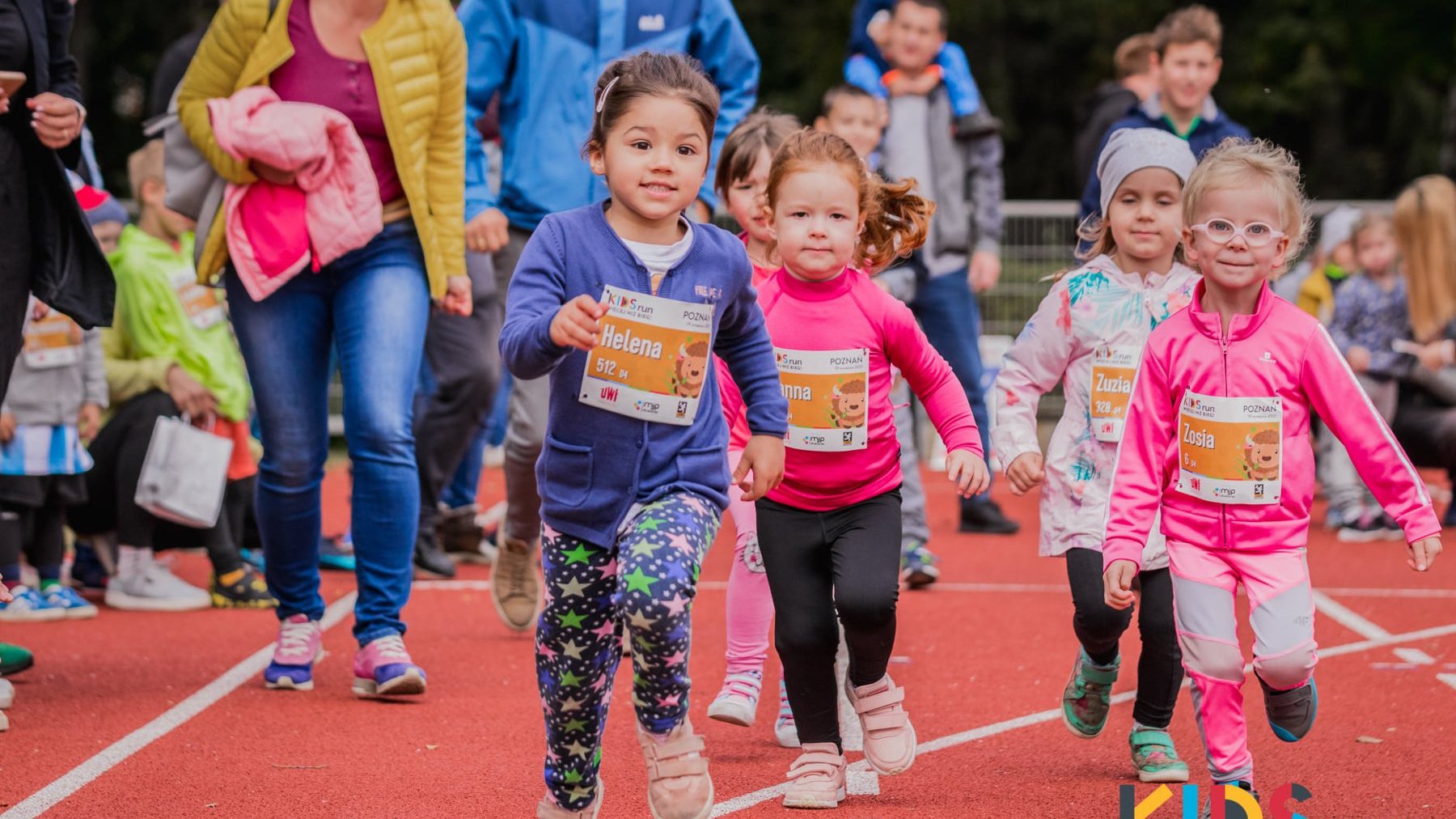 Galeria zdjęć przedstawia grupe dziecie biegnącą po bieżni podczas imprezy Kids Run.