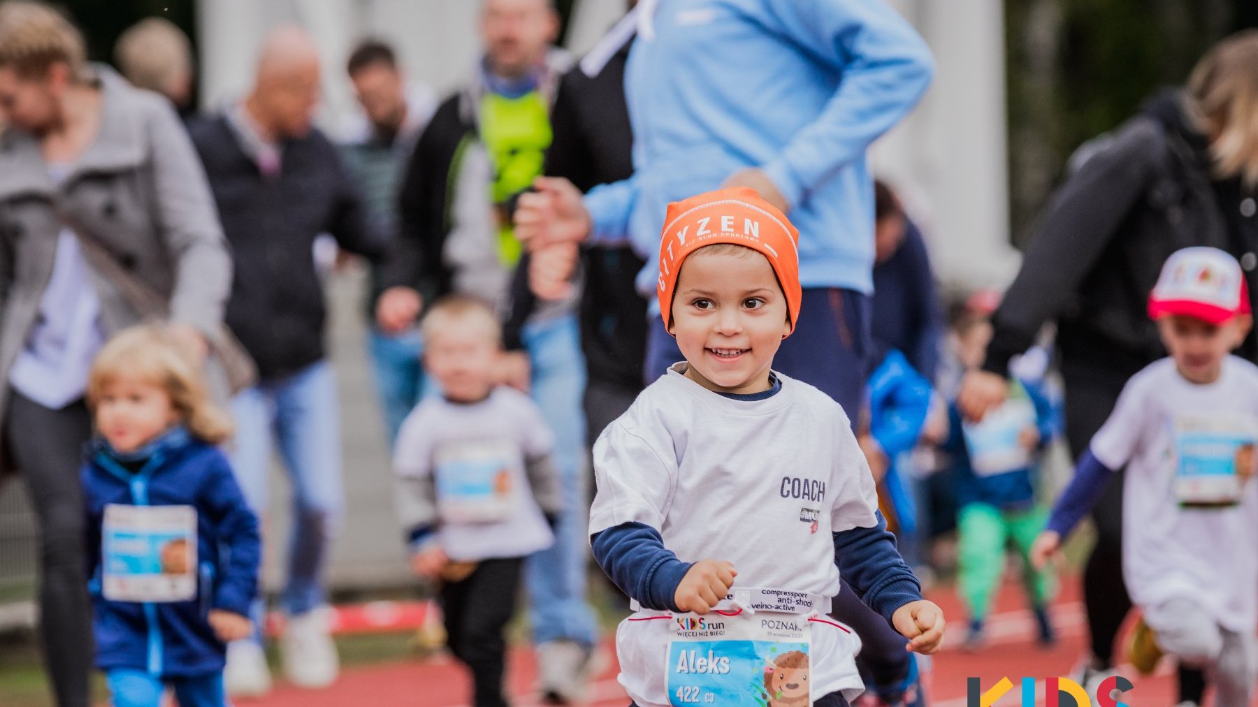 Galeria zdjęć przedstawia grupe dziecie biegnącą po bieżni podczas imprezy Kids Run.