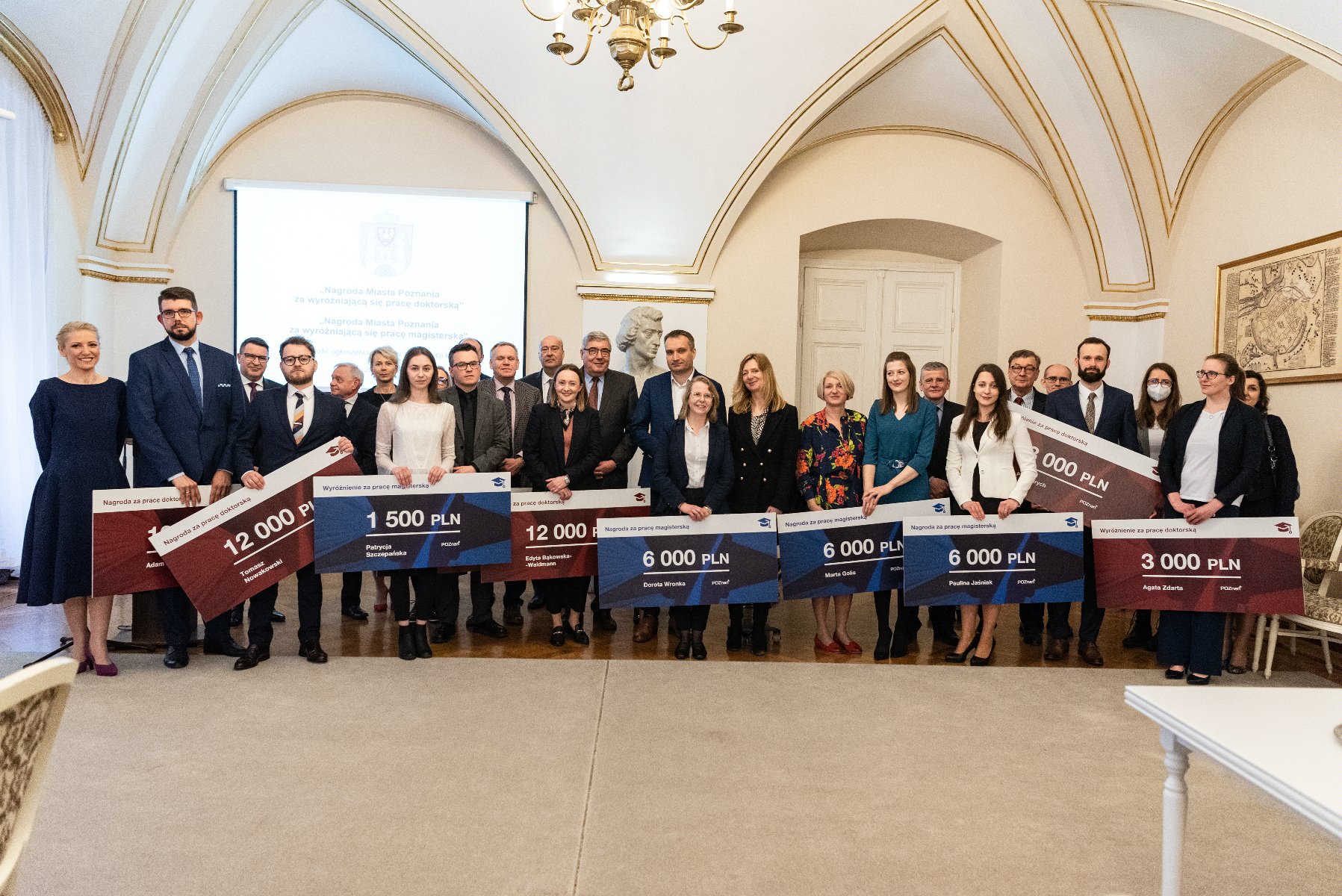 Galeria zdjęć przedstawia wręczenie nagród w sali urzędu miasta. Widać na nich wiceprezydenta Poznania i przewodniczącego Rady Miasta Poznania oraz laureatów. - grafika artykułu