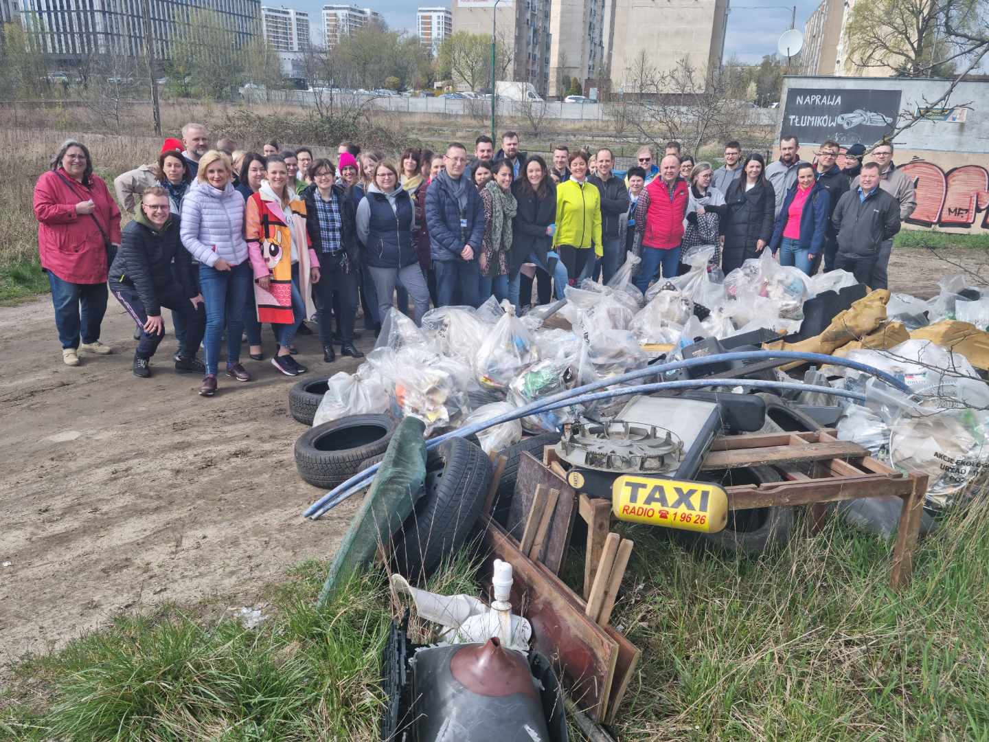 Zdjęcie przedstawia zbiorowe zdjęcie pracowników urzędu. Na pierwszym planie znajduje się góra śmieci. - grafika artykułu