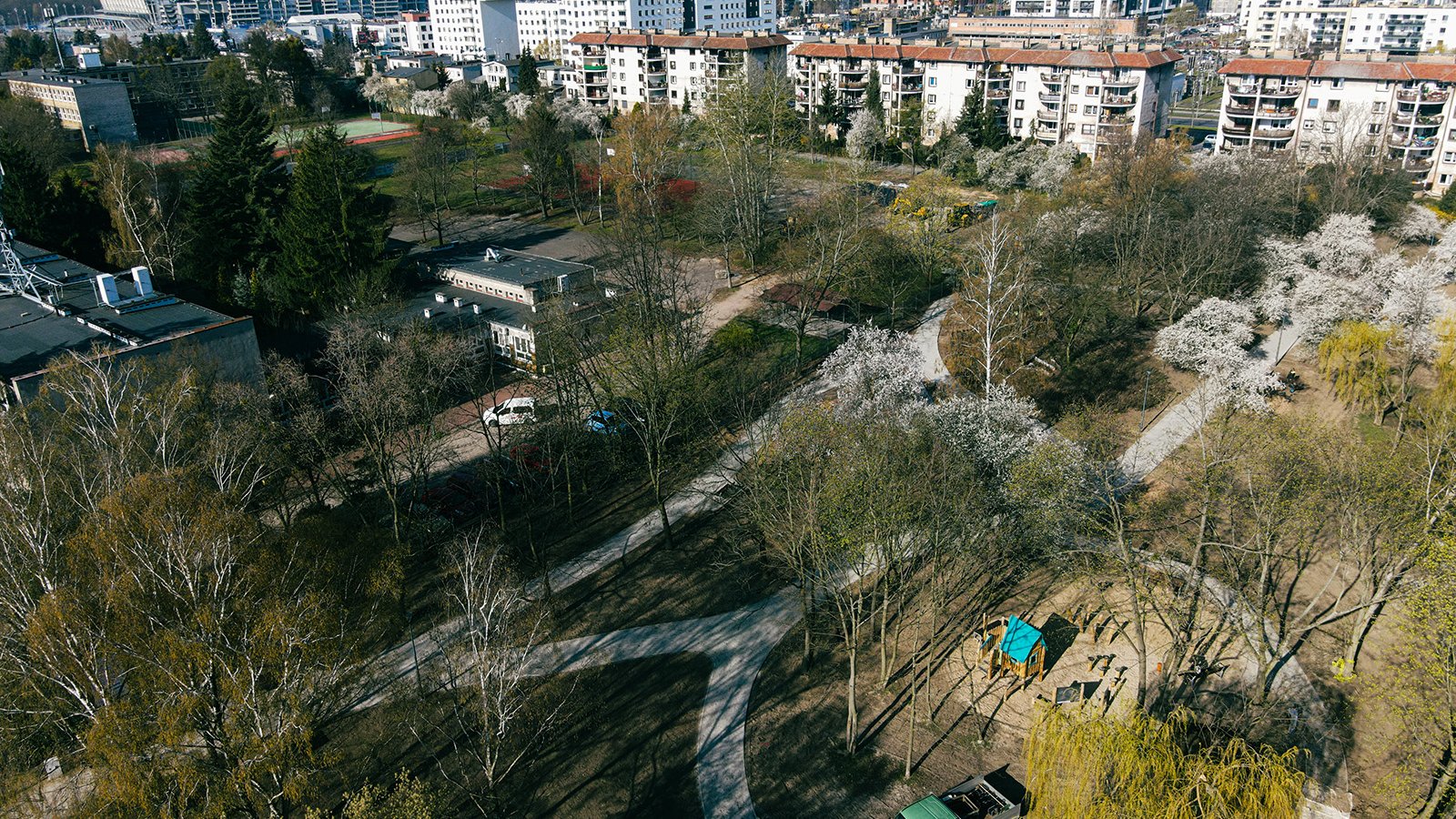 Zdjęcie przedstawia nowy zieleniec z lotu ptaka. W oddali widać tez budynki mieszkaniowe.