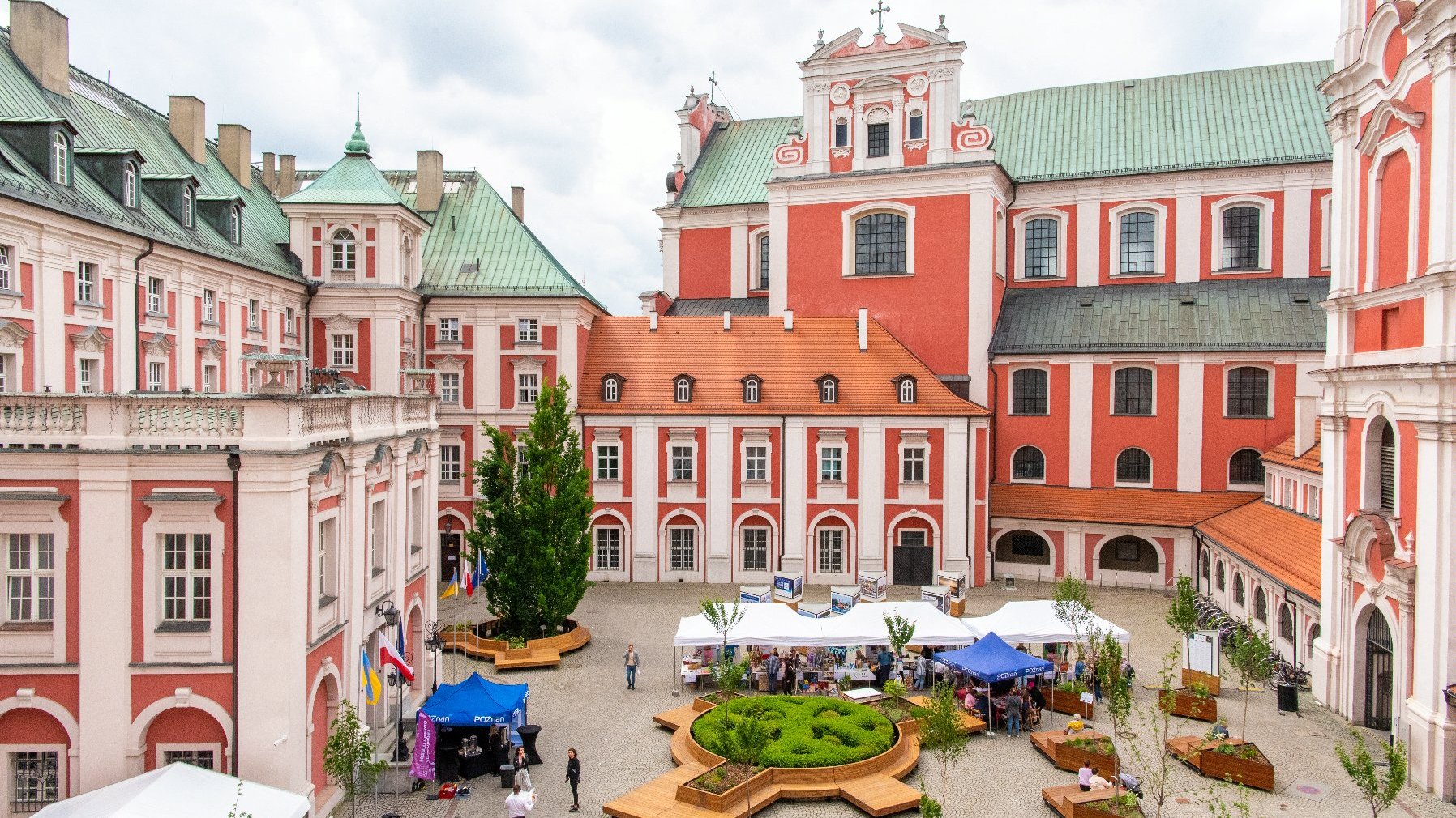 Zdjęcie przedstawia dziedziniec urzędu miasta z góry. Widać na nim namioty i ludzi, a także ławki i rośliny.