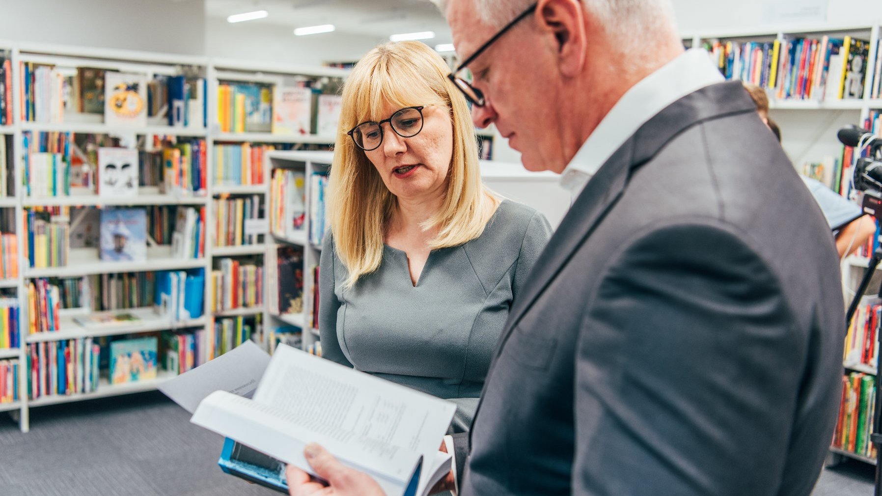 Na zdjęciu prezydent Poznania z książką w ręku, rozmawia z dyrektorką biblioteki, w tle regały z książkami