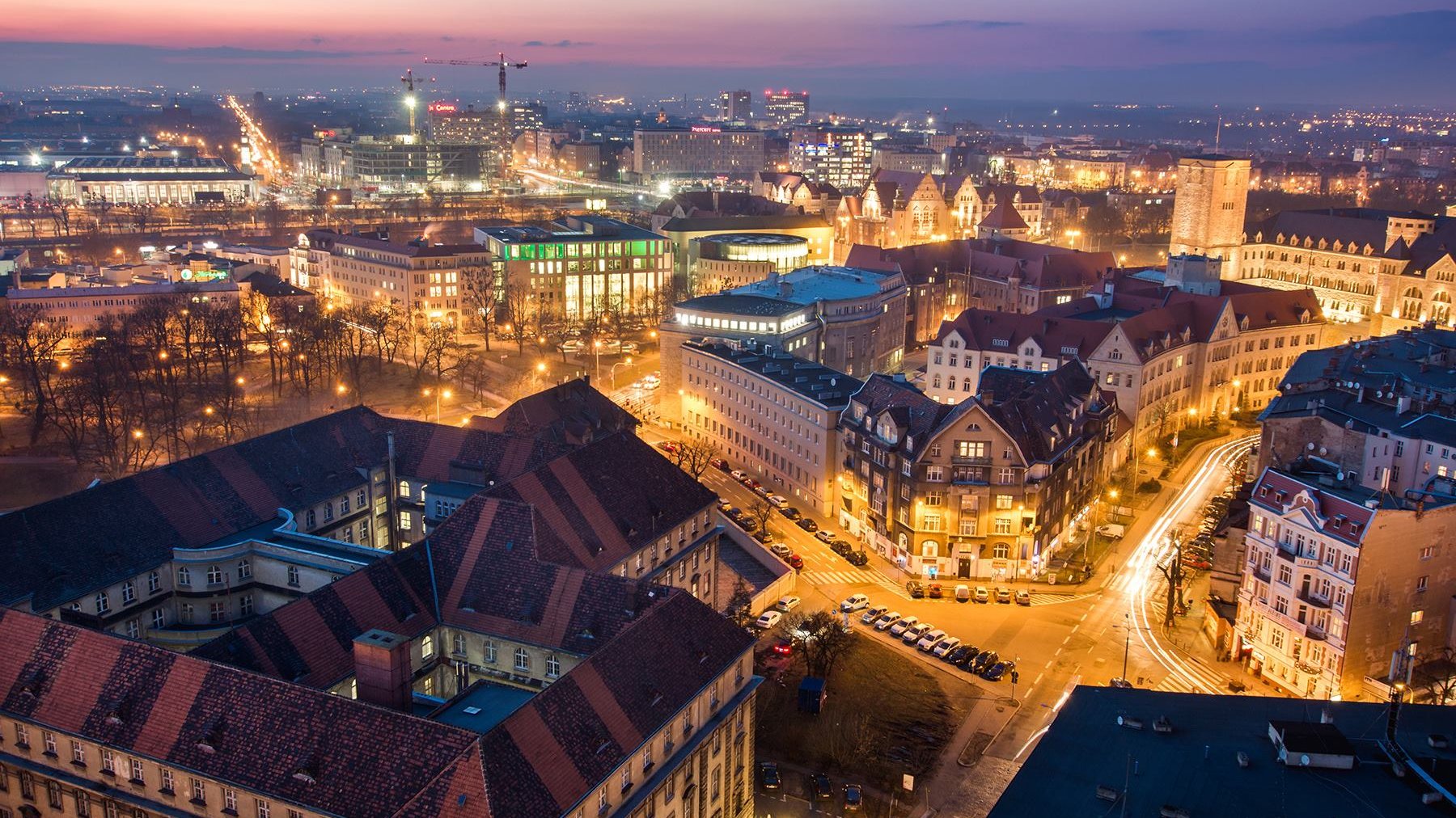 Na zdjęciu panorama Poznania o zmroku, widać dachy kamienic i Okrąglak