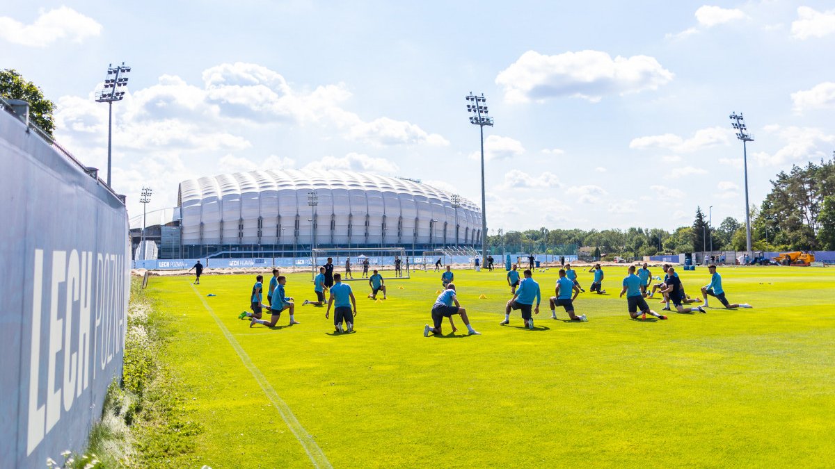 Na zdjęciu piłkarze Lecha Poznań na boisku rozgrzewają się, w tle stadion.