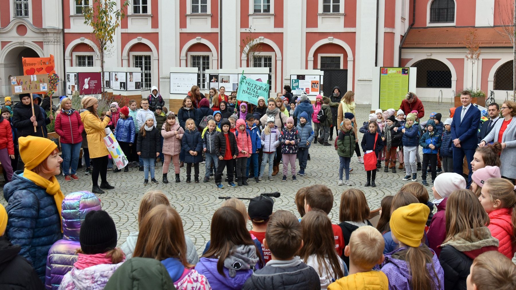 Na zdjęciu dzieci zebrane na dziedzińcu urzędu miasta, niektóre trzymają transparenty