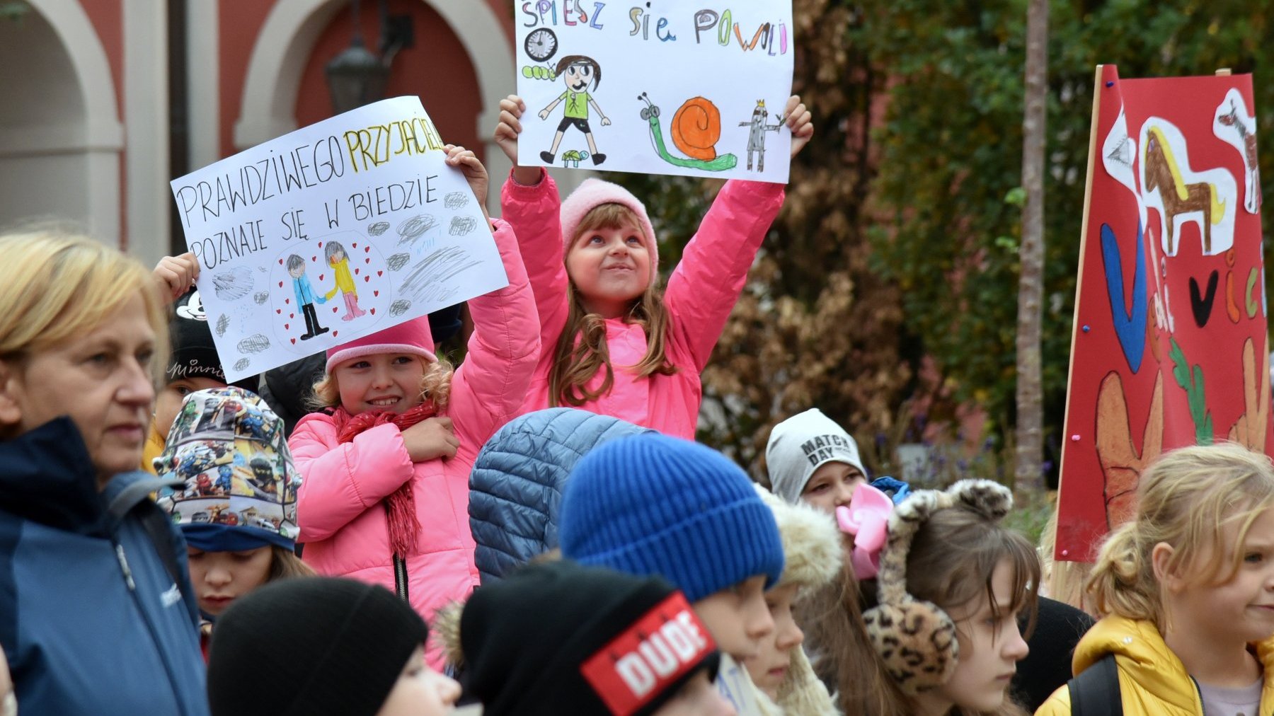 Na zdjęciu dzieci trzymające plakaty w wyciągniętych w górę rękach