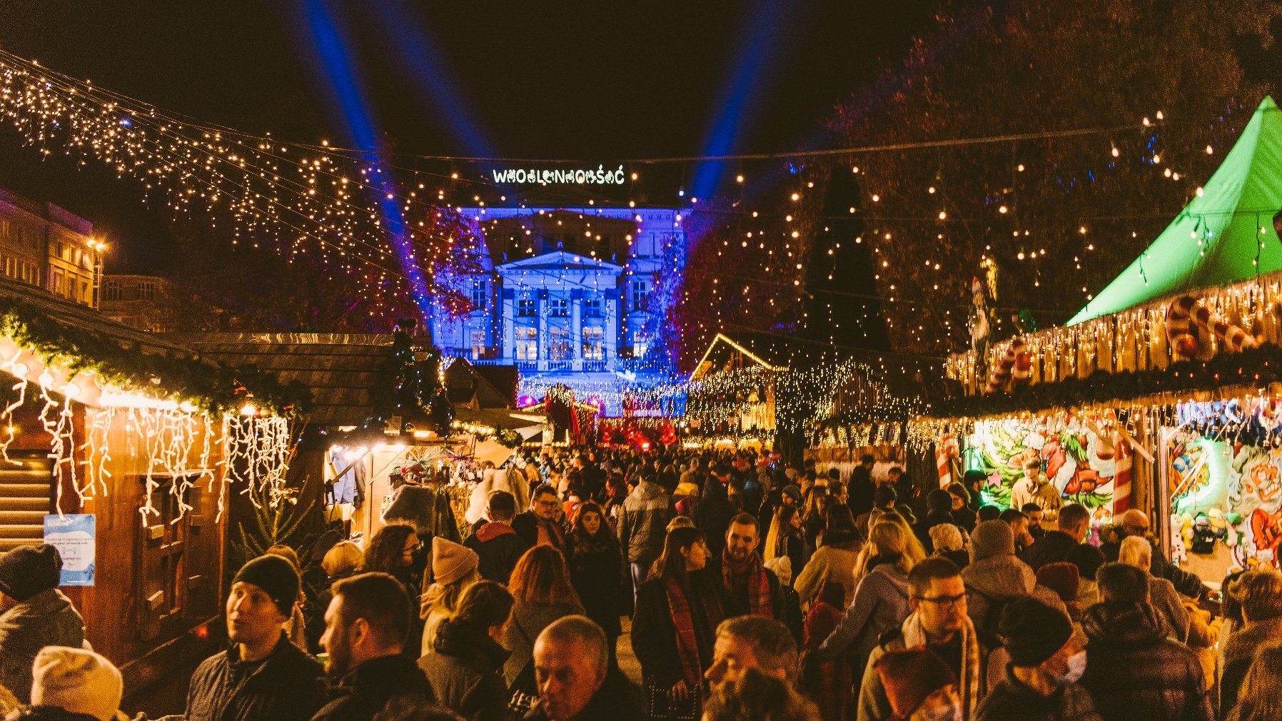 Zdjęcie przedstawia plac Wolności po zmroku udekorowany girlandami lampek. Przestrzeń placu jest wypełniona ludzmi.