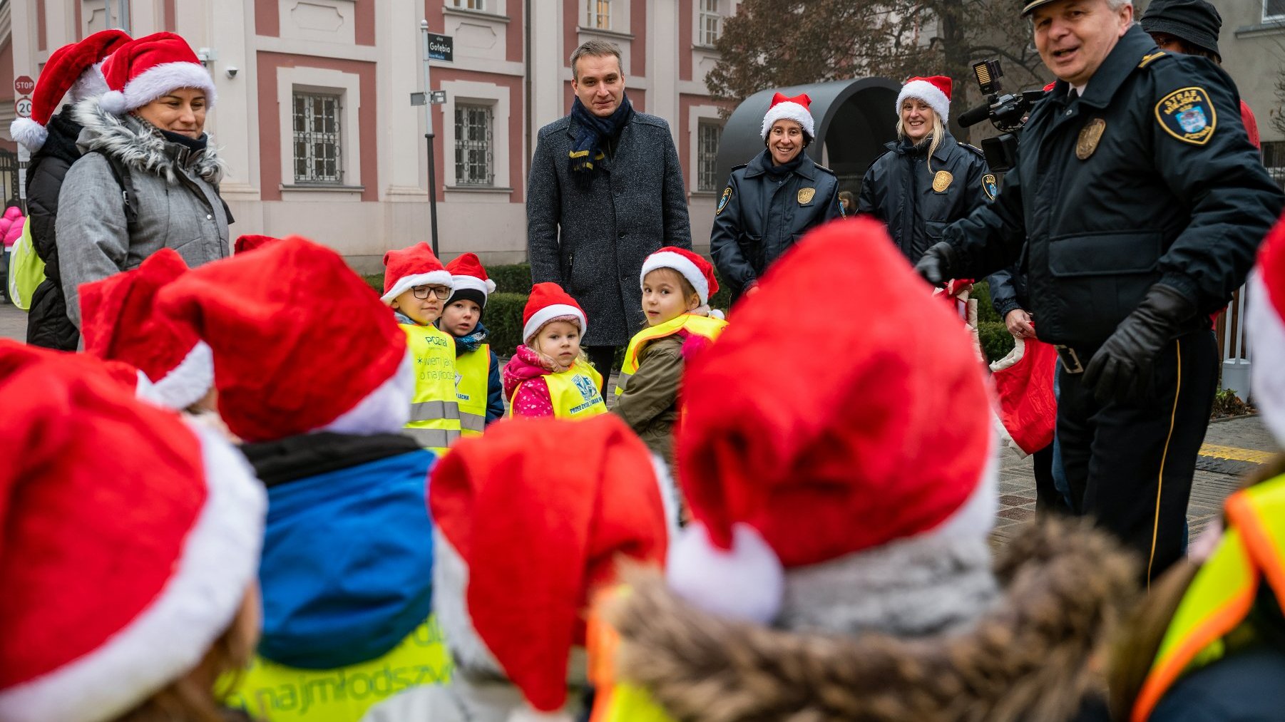 Galeria zdjęć przedstawia grupę dzieci i dorosłych dekorujących rzeźbę koziołków w mikołajkowe stroje.