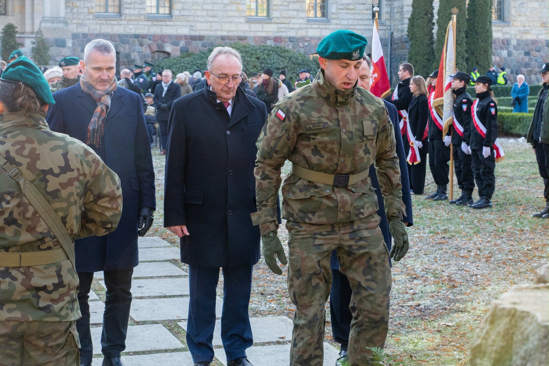 Na zdjęciu mężczyźni składający kwiaty, na pierwszym planie żołnierz - grafika artykułu