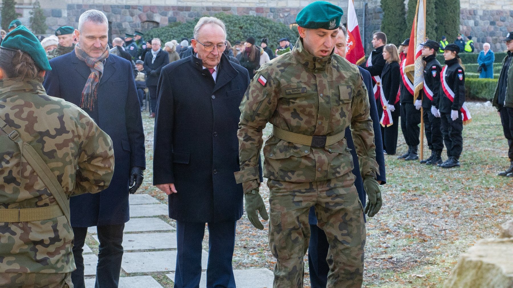 Na zdjęciu mężczyźni składający kwiaty, na pierwszym planie żołnierz