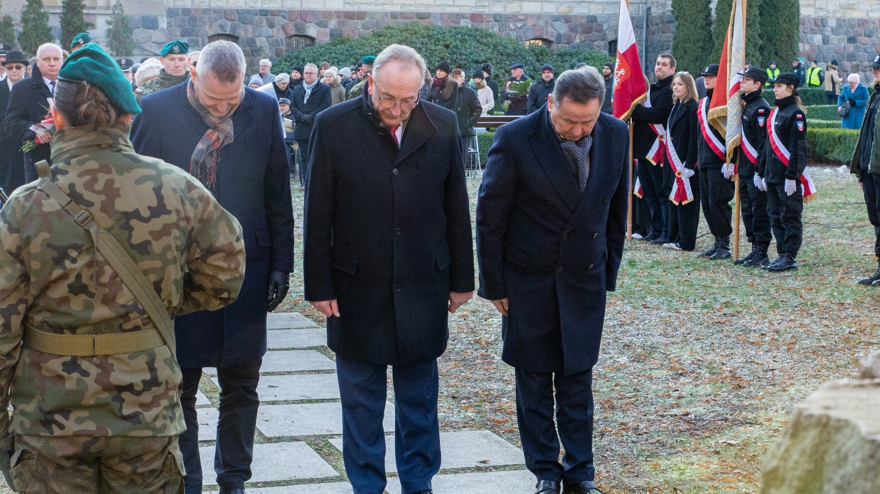 Na zdjęciu trzej mężczyźni w pokłonie, w tle poczet sztandarowy