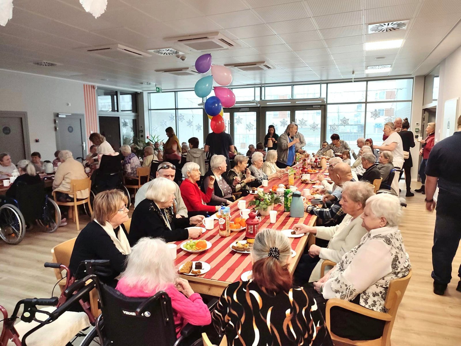 Na zdjęciu duża grupa seniorów i seniorek siedzących przy stołach - grafika artykułu