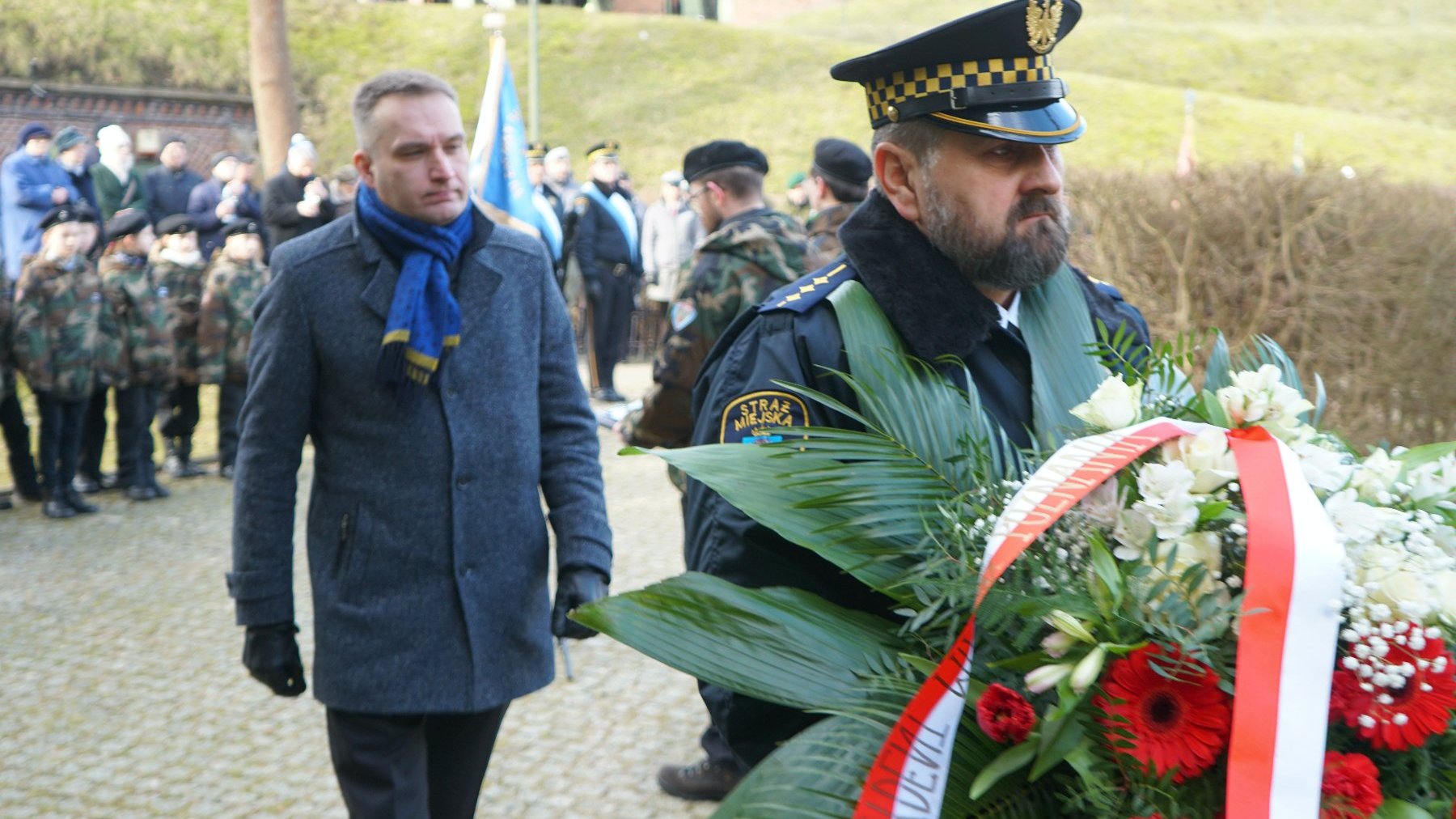 Na zdjęciu zastępca prezydenta Poznania składajacy kwiaty, przed nim strażnik miejski z wiązanką